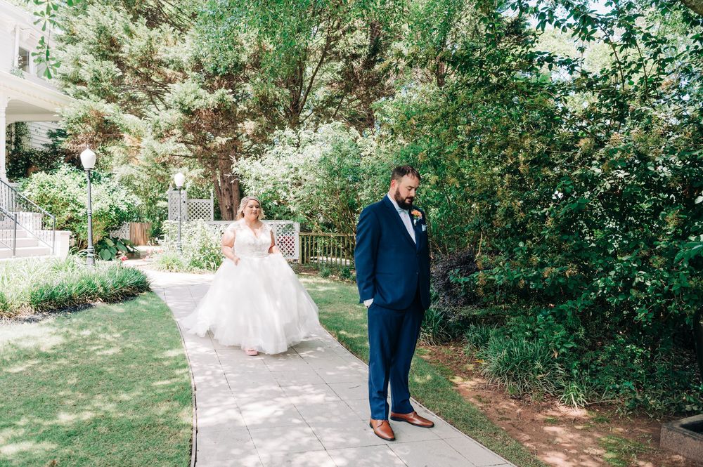 A couple walks through a lush garden path surrounded by greenery on their wedding day.