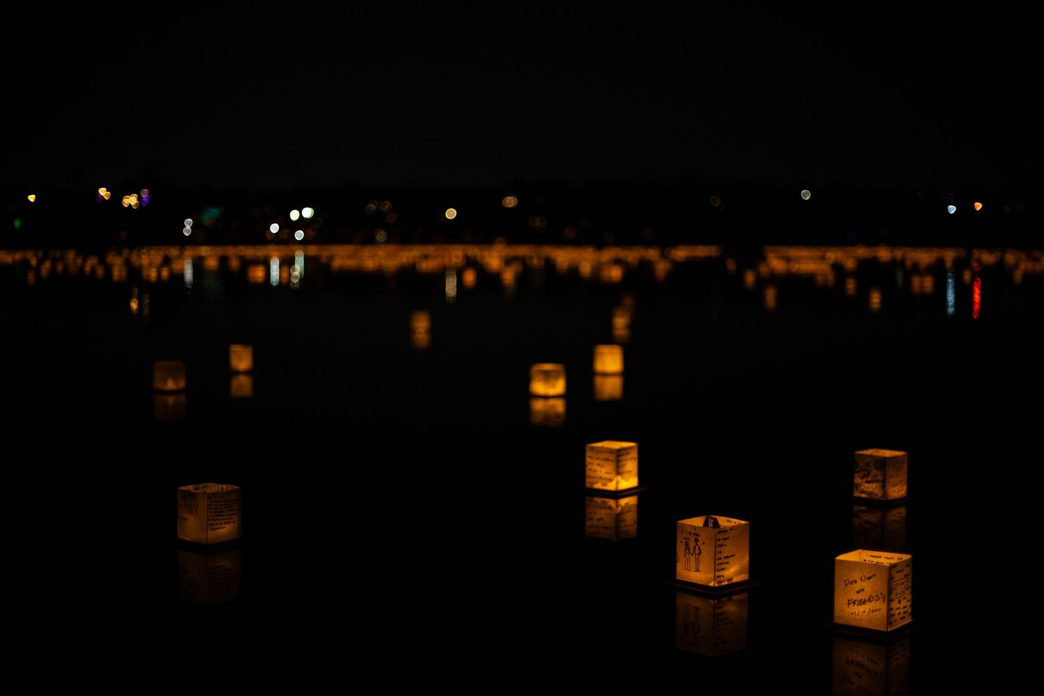 Glowing paper lanterns illuminate a dark lakeside path creating a peaceful nighttime atmosphere with reflections on the water.