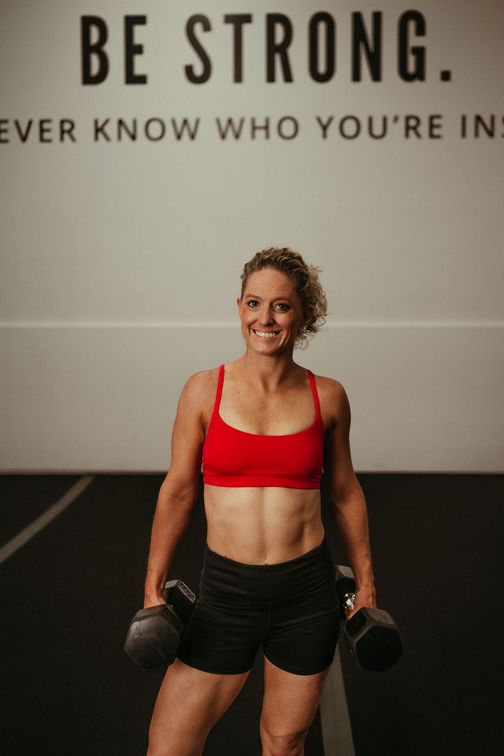 An athlete in red sports bra and black shorts performs dynamic exercises in a light-colored studio setting.