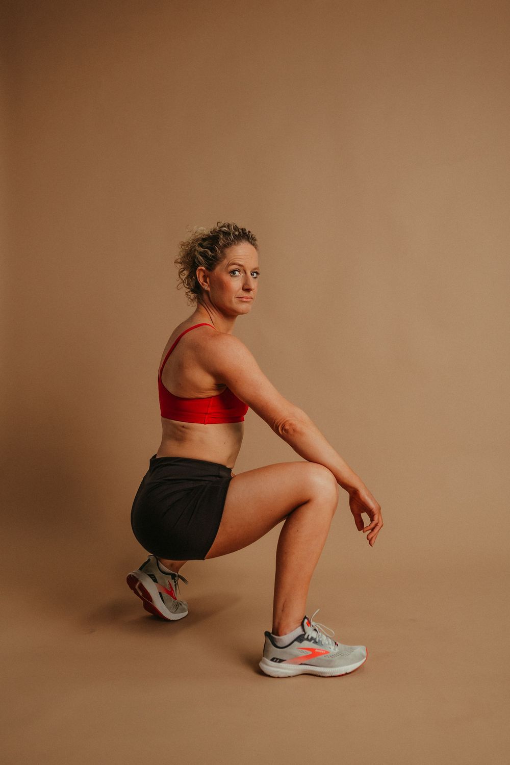 Person in athletic wear demonstrates squatting positions in a sequence against warm brown backdrop.