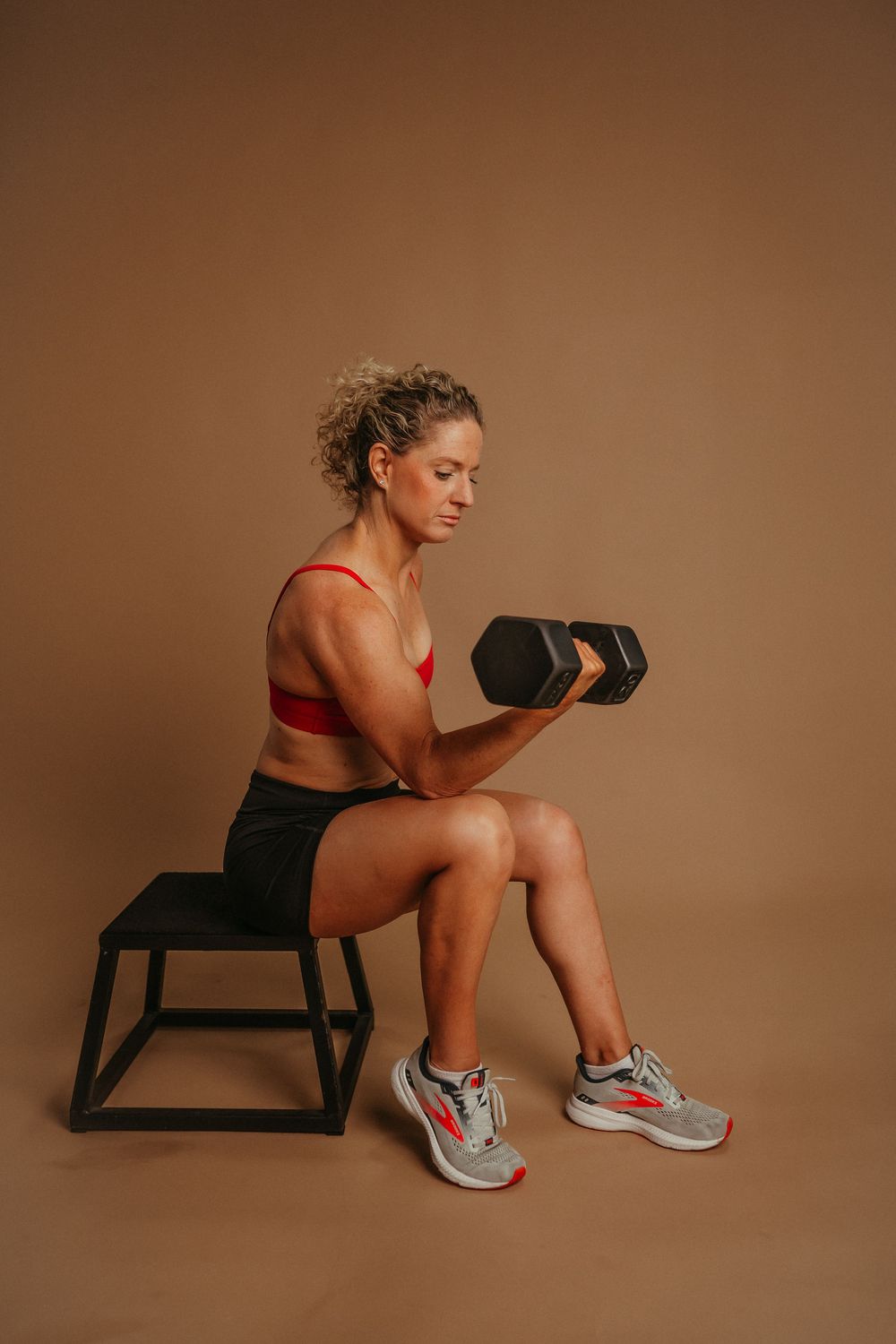 An athlete performs stretching exercises on a small black bench against a warm brown backdrop.