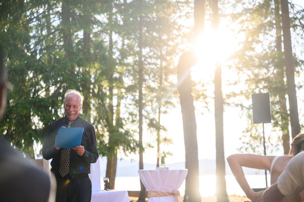 Two people visible amongst tall evergreen trees at sunset as golden light streams through the forest canopy.