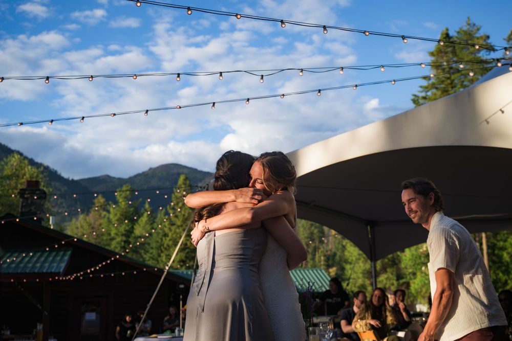 Outdoor reception at dusk with string lights and mountain views while people dance beneath a canopy.