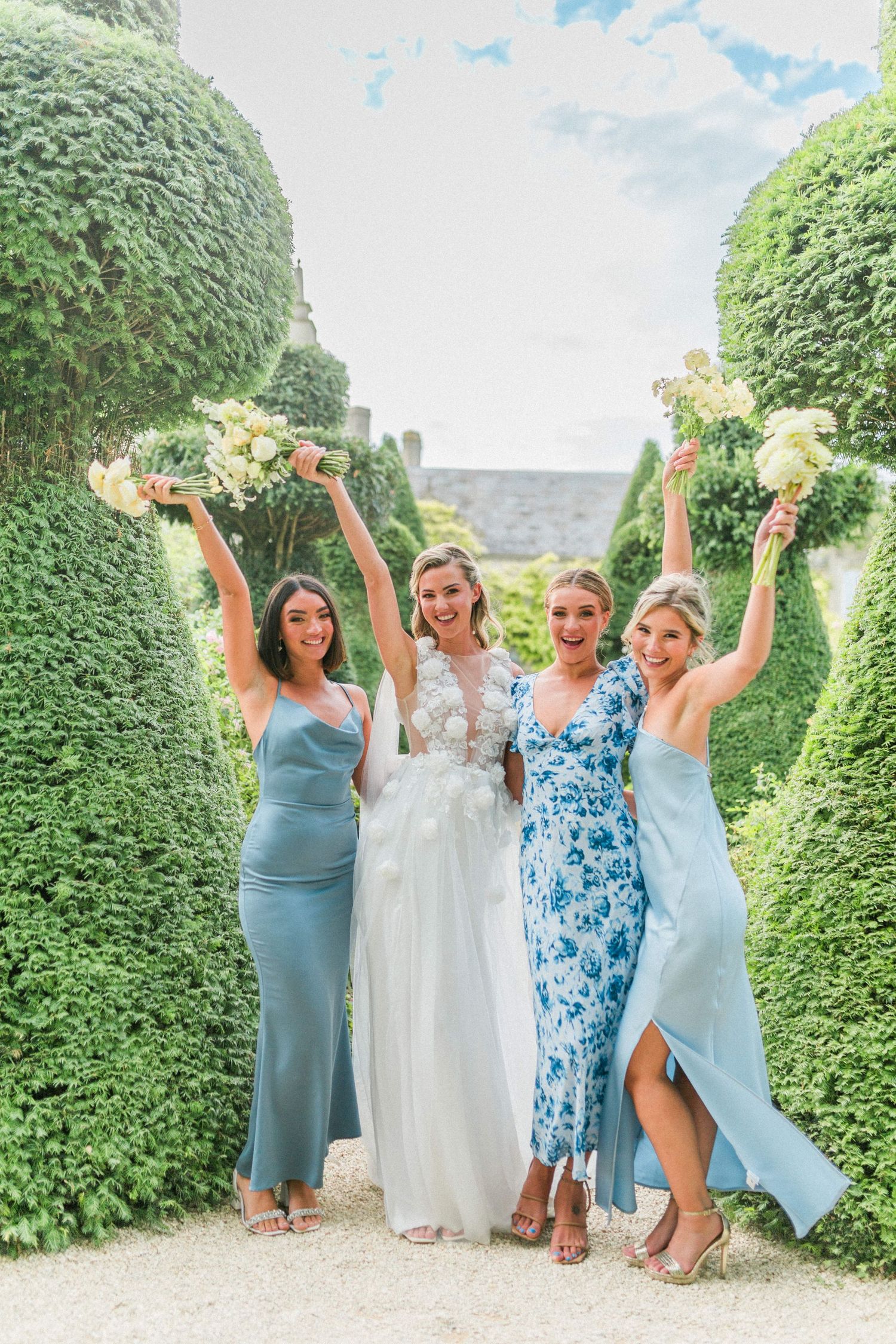 A group of bridesmaids in mixed blue dresses pose with the bride at Euridge Manor in Wiltshire by Hayley Elizabeth Photography