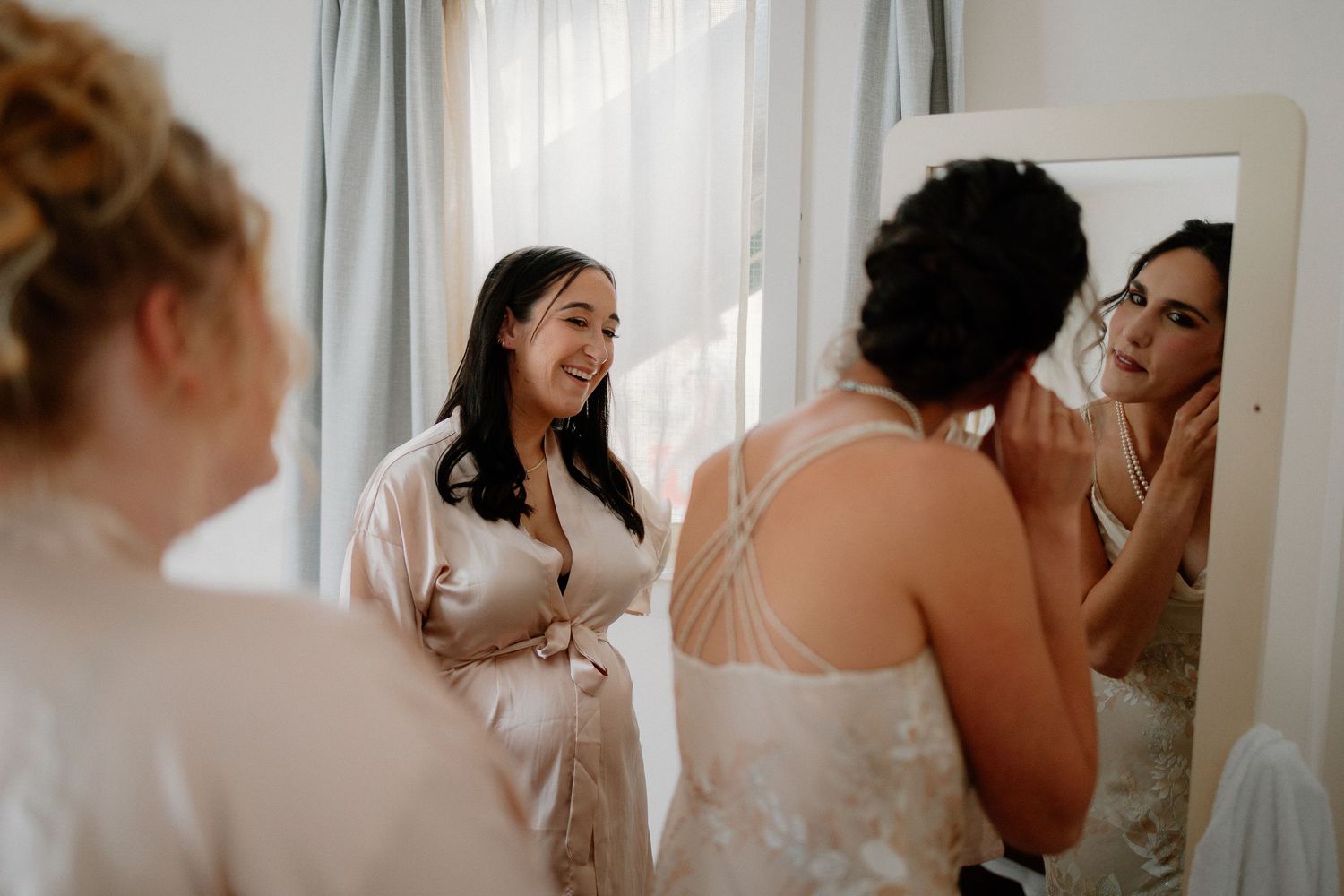 People sharing joyful moments while getting ready in a bright room with a mirror and natural light.