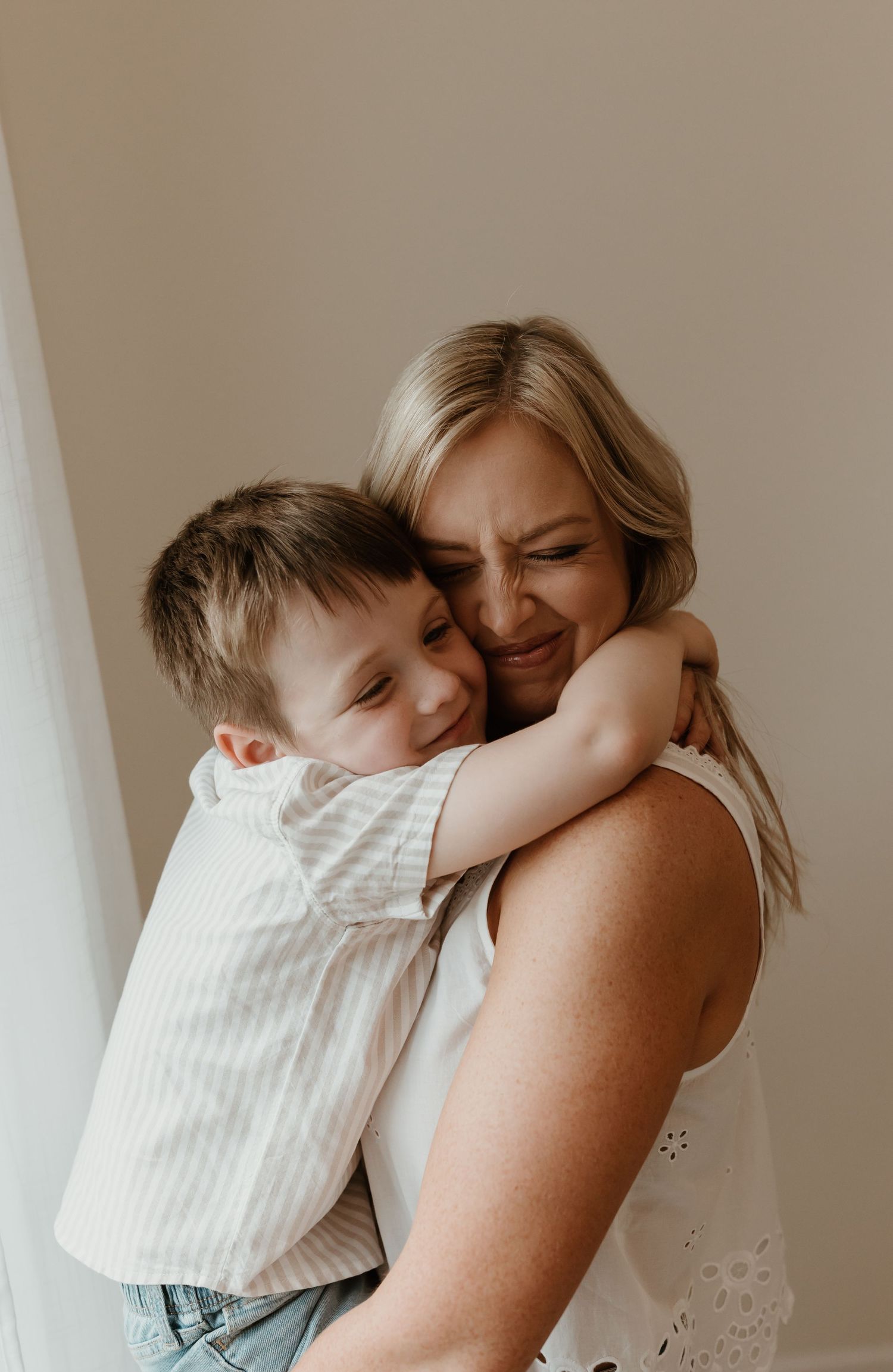 A heartwarming embrace shared between parent and child, both smiling with pure joy against a neutral backdrop.