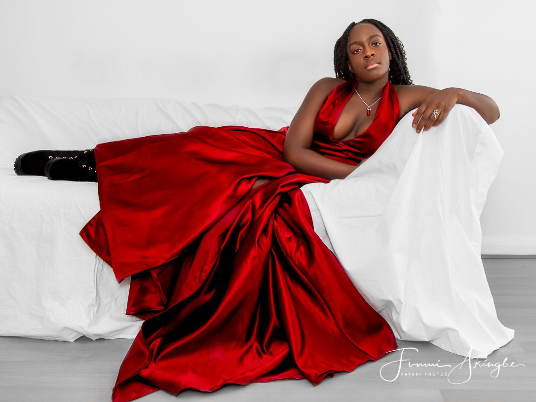 Reni wearing elegant red prom dress and edgy black boots, reclining against a white backdrop during an at-home photoshoot.