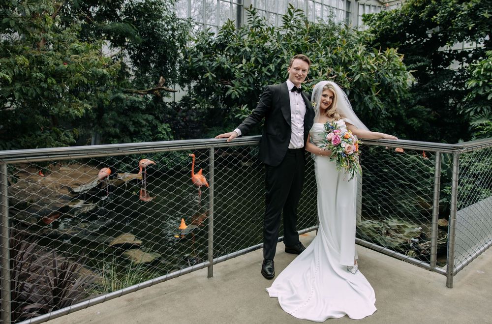 A newlywed couple poses together on a balcony overlooking a garden with decorative railing.