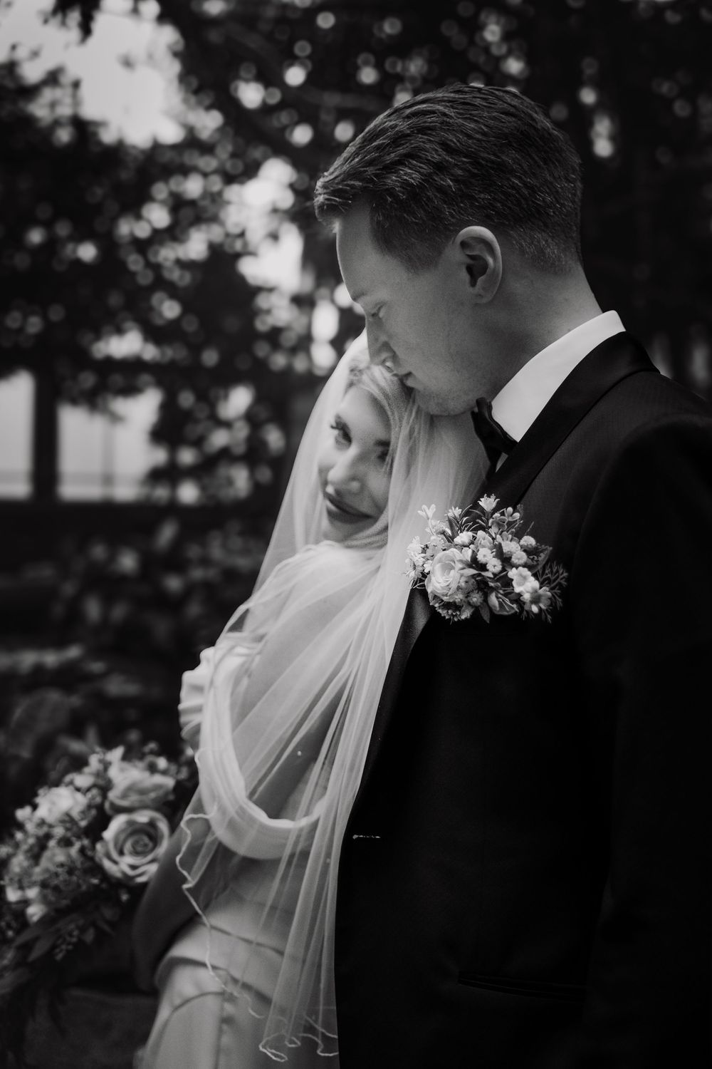 A romantic black and white wedding portrait capturing a tender moment between a bride and groom outdoors.