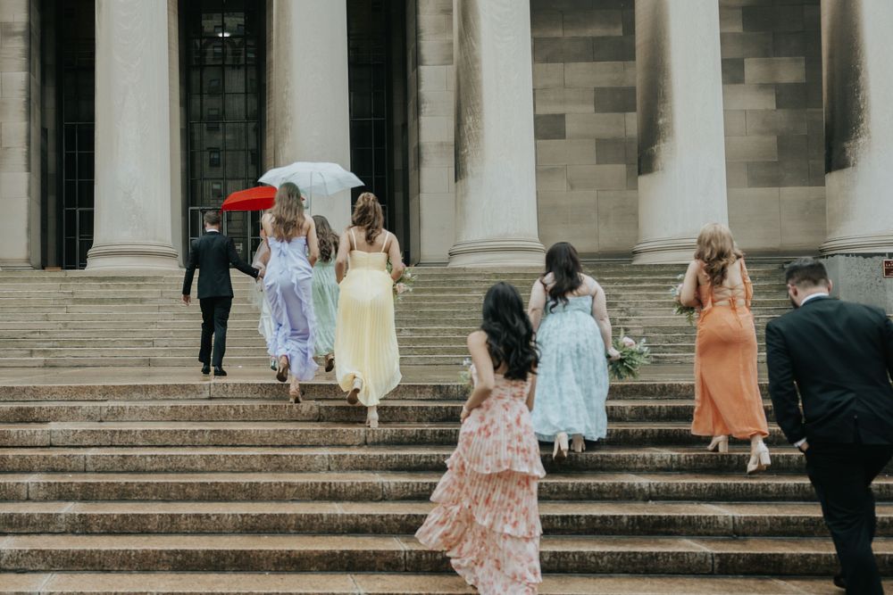 Group of people in colorful dresses walking up stone steps of a classical building on an overcast day.