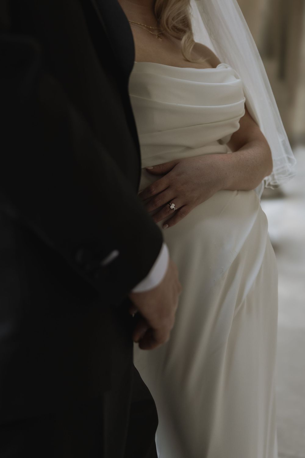 A tender moment between newlyweds showing hands embracing through elegant white wedding dress and black suit.