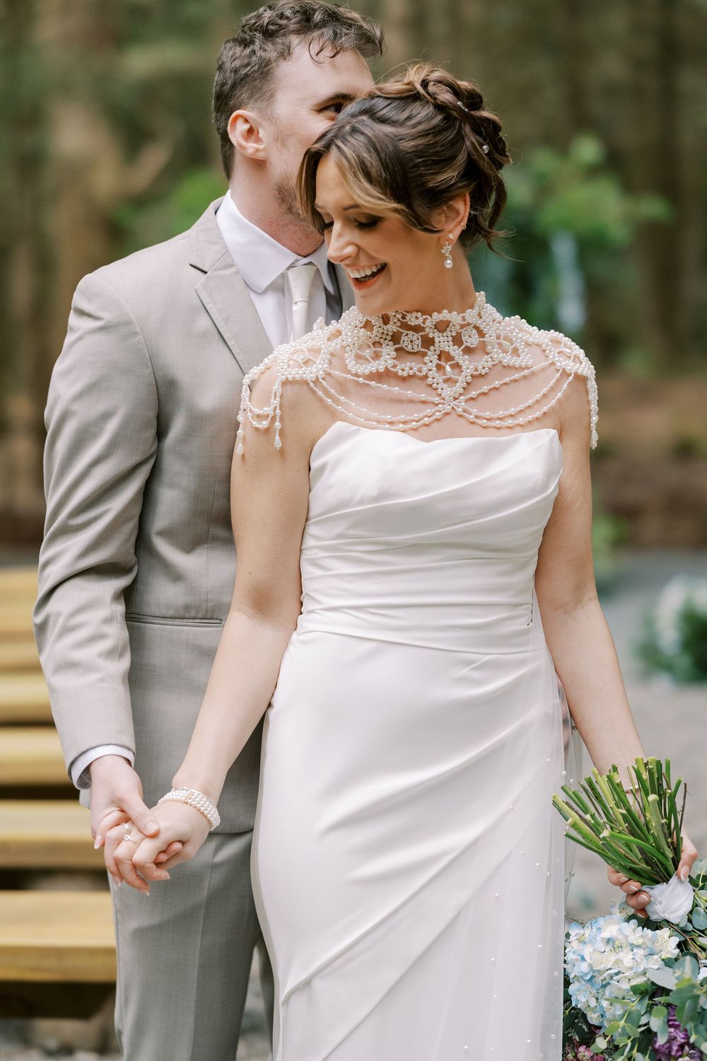 A romantic wedding moment features a light grey suit and an elegant white dress with intricate beaded neckline detail at Windham Manor.