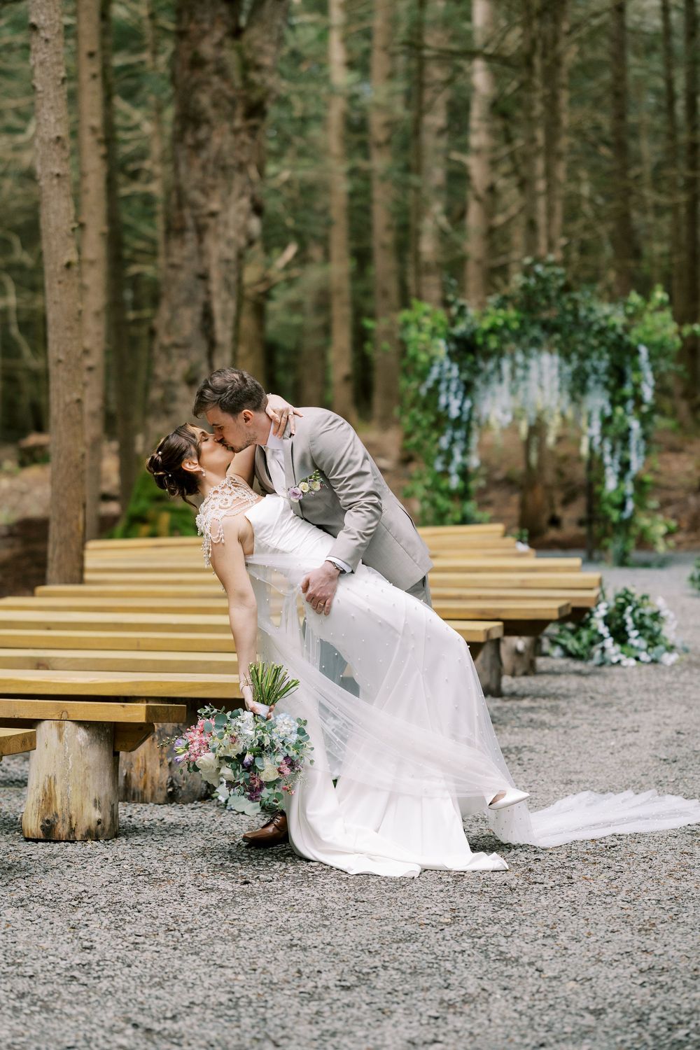 Romantic outdoor forest wedding with wooden benches and floral arch decor in a woodland setting at Windham Manor.