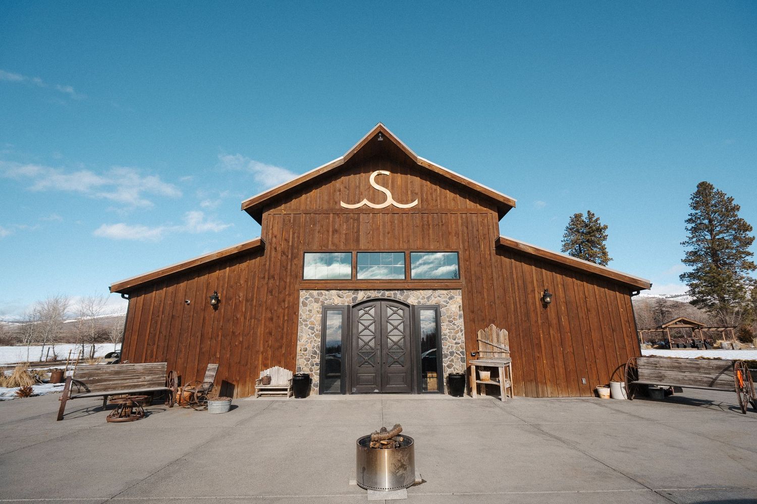 A rustic brown wooden barn wedding venue with decorative front doors and 'SJ' lettering under clear blue skies.