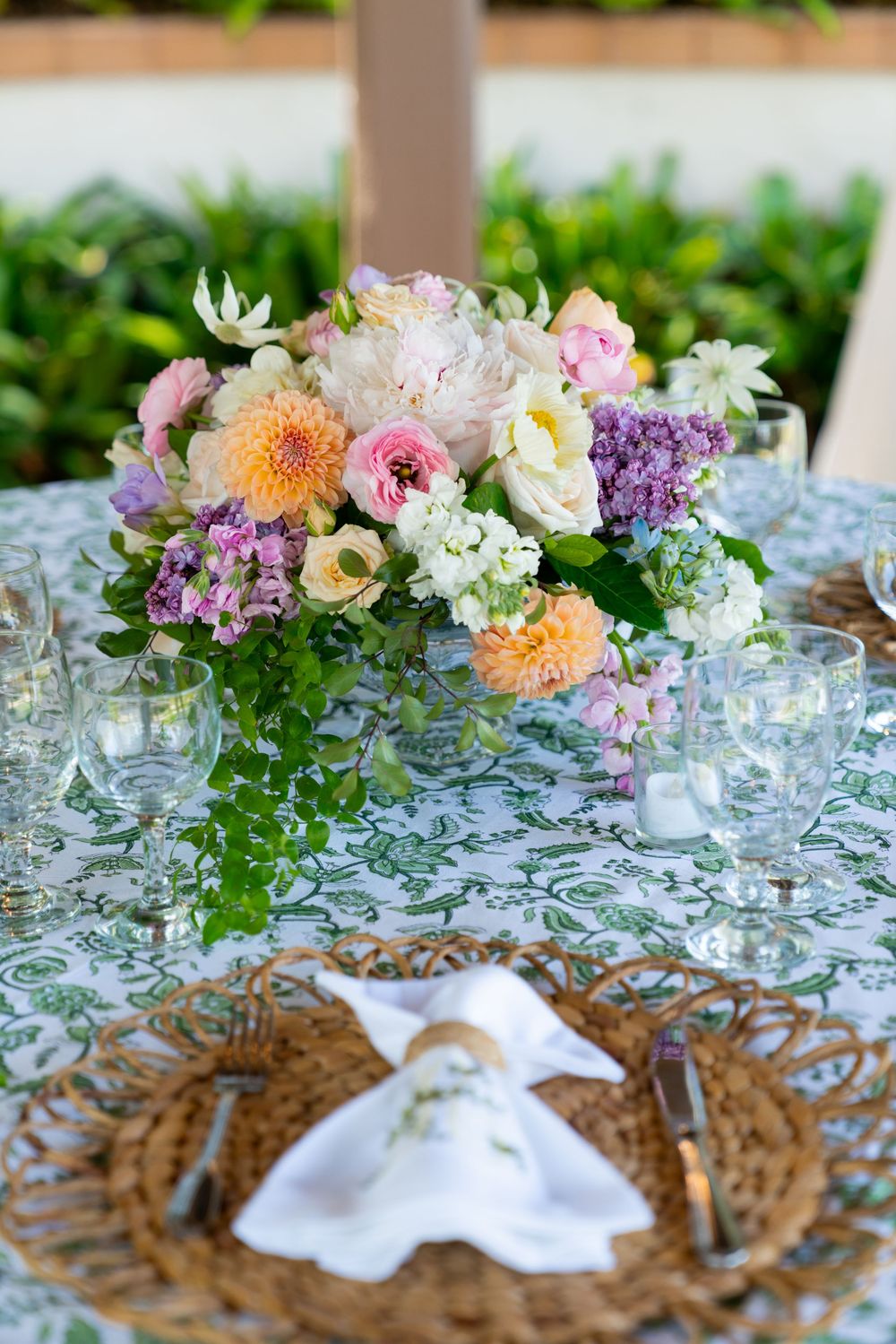 A romantic table setting with a colorful floral centerpiece and woven charger plates on a patterned tablecloth.