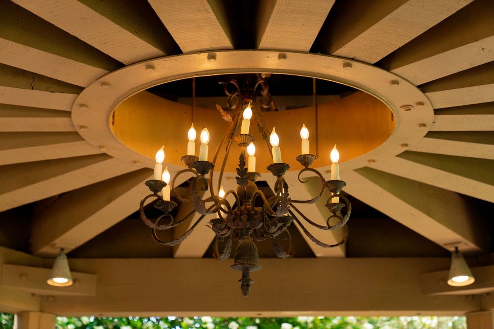 An elegant chandelier with glowing candle-style lights hangs from a wooden beam ceiling with radiating patterns.
