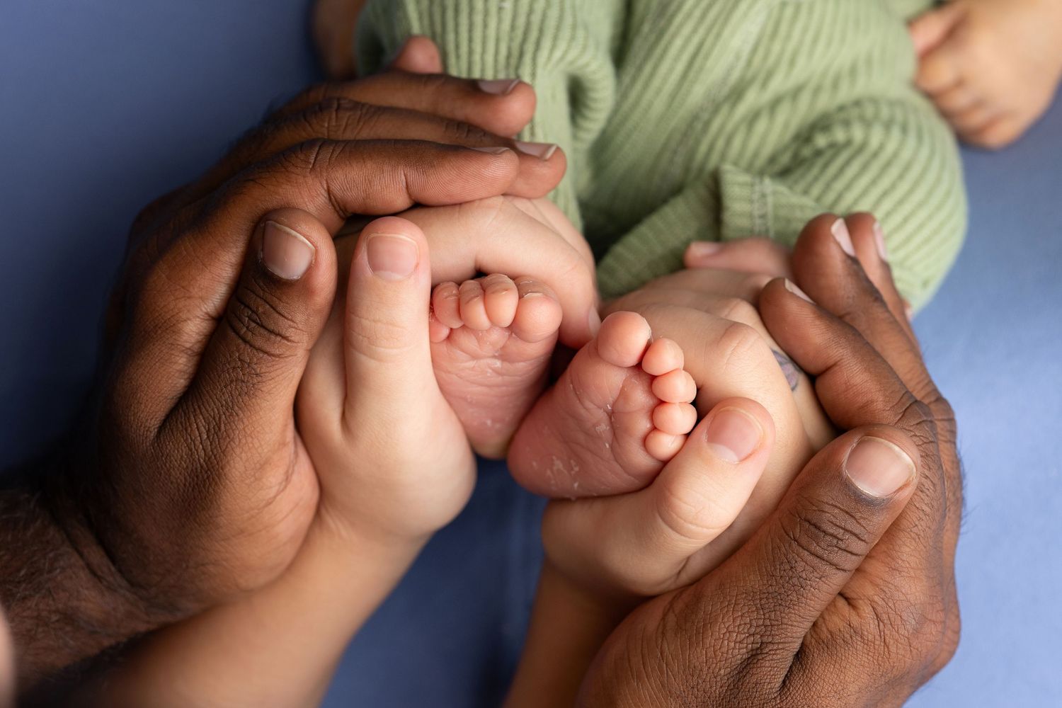 Tiny newborn baby feet gently held by adult hands against a soft blue background.
