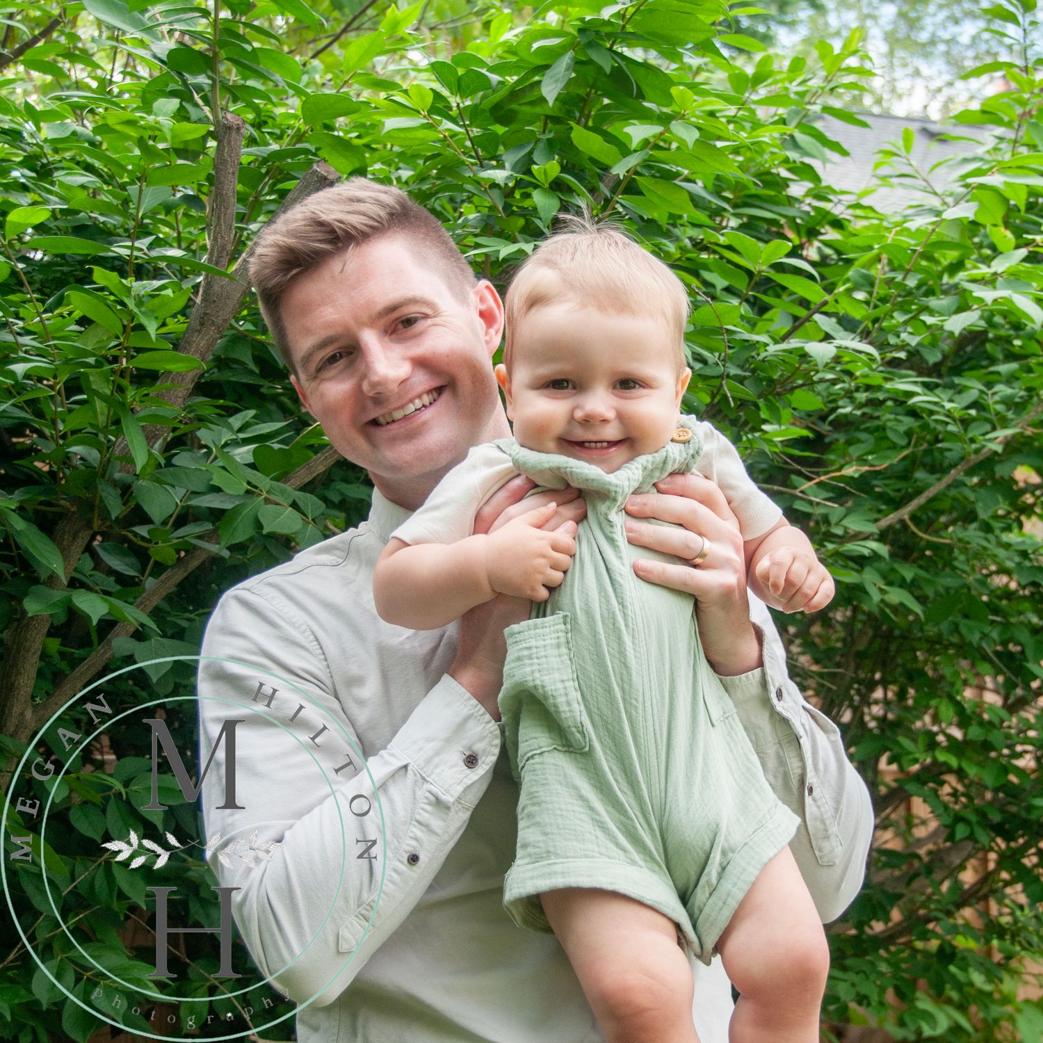 Photograph of a dad and little boy sharing a joyful moment together against leafy green foliage in summer.