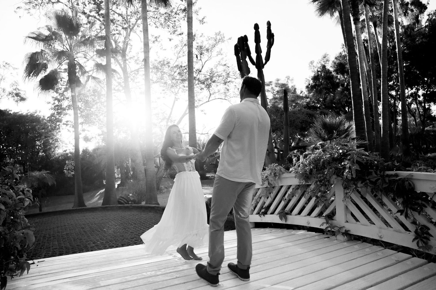 A couple celebrates on a wooden deck surrounded by palm trees and tropical foliage at sunset during their wedding ceremony.
