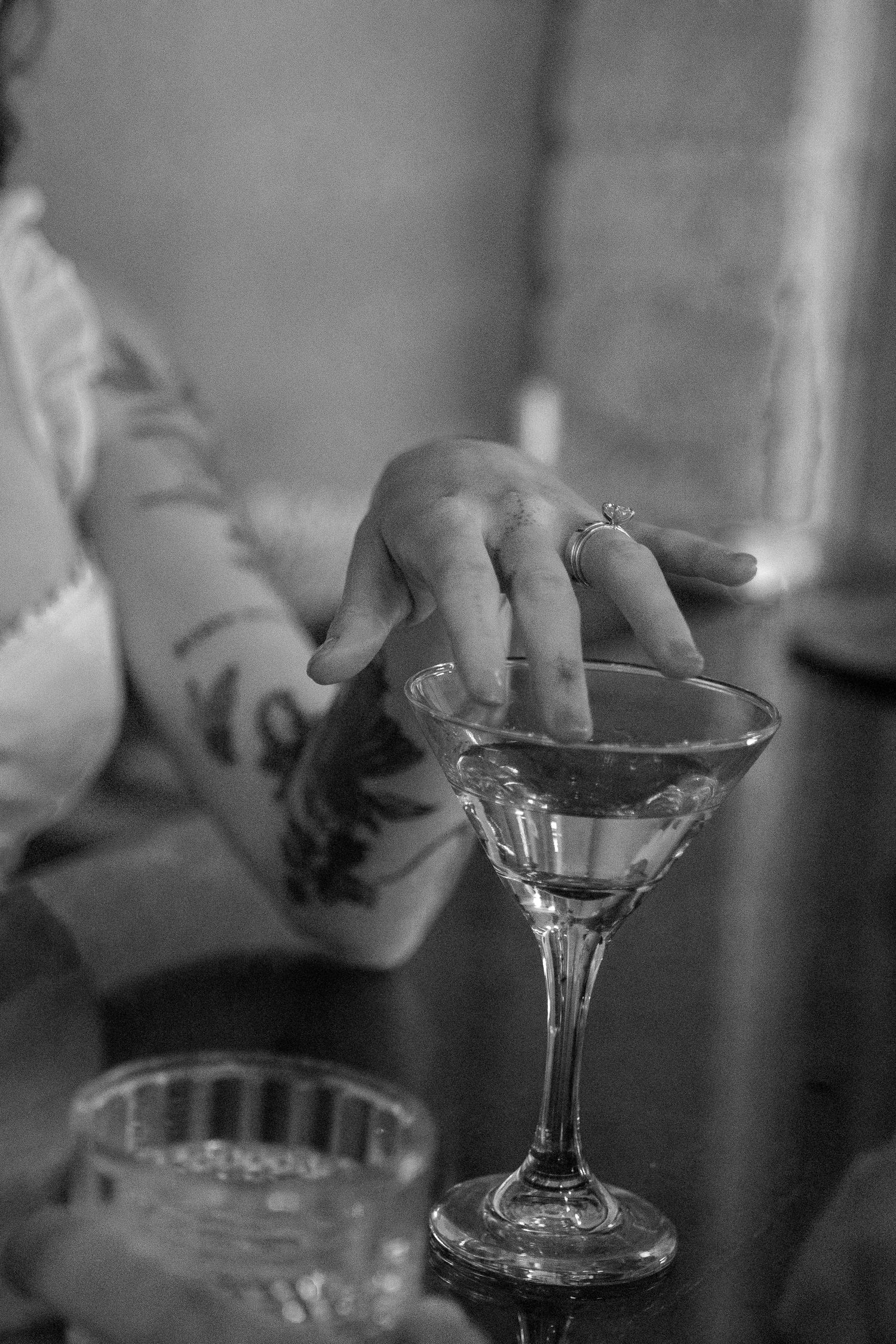 Close-up black and white photo of a hand with tattoos holding a martini glass.