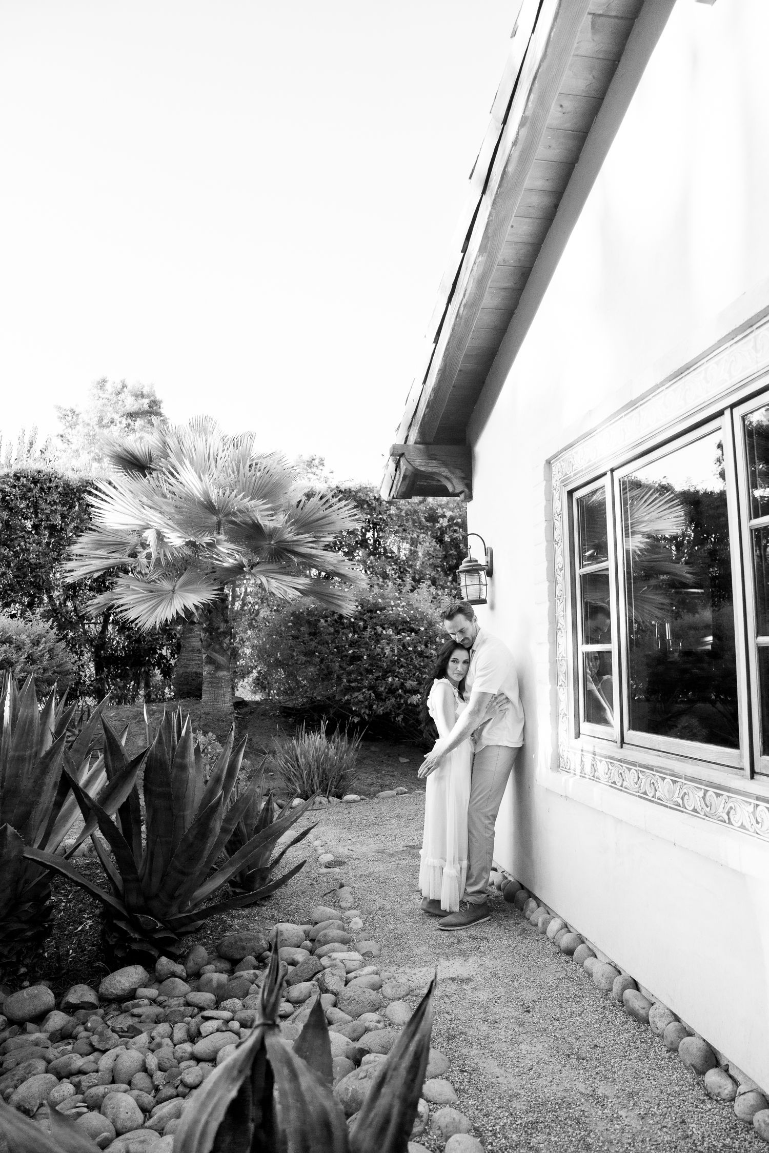 Black and white photo of a garden landscape with palm trees and succulents alongside a white house exterior.
