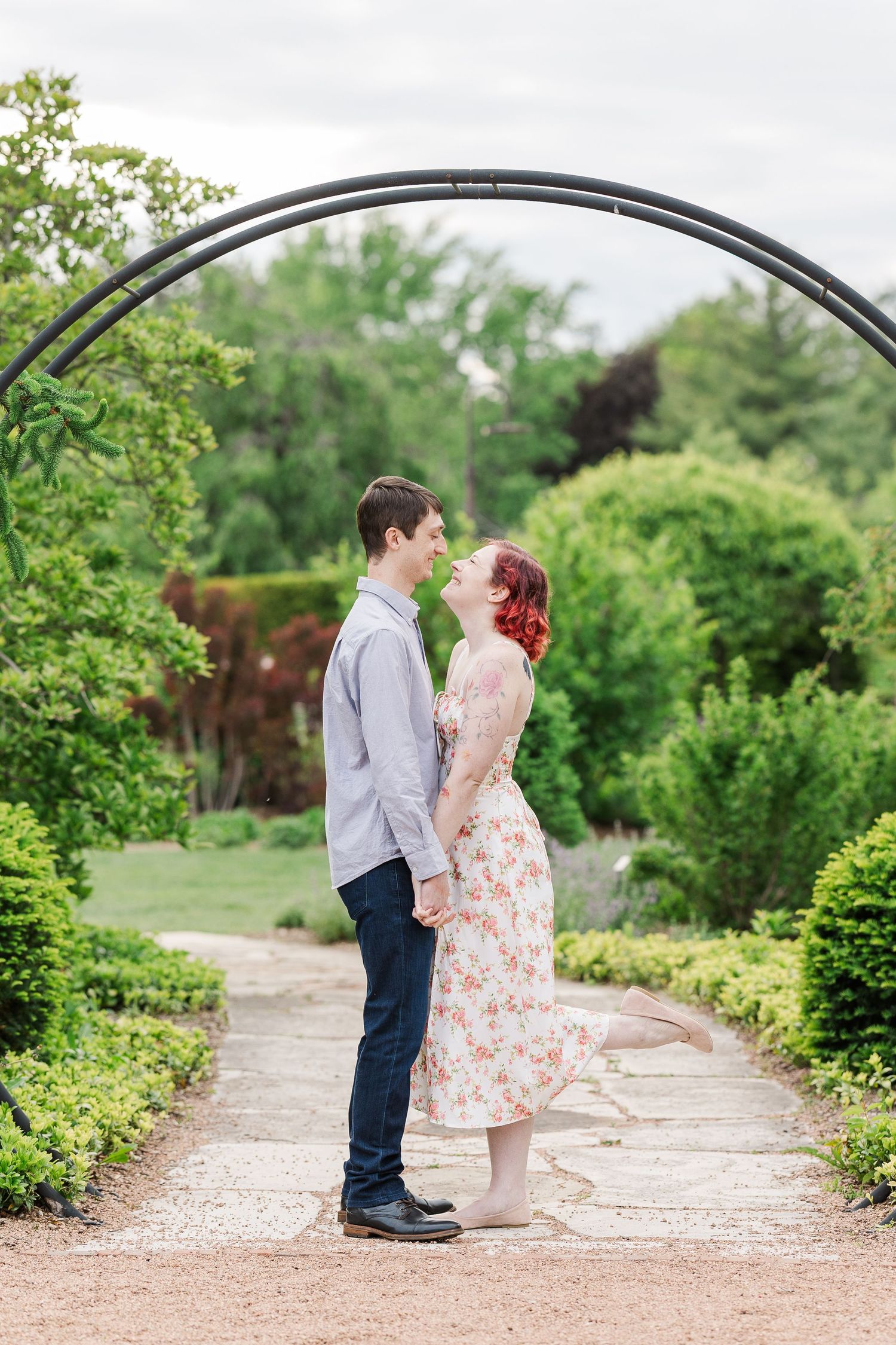 A couple shares a romantic moment under a garden archway surrounded by lush greenery and flowering plants at Cantigny Park