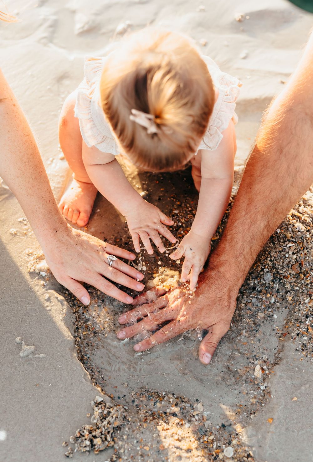 Hands playing in the sand together on a sunlit beach.