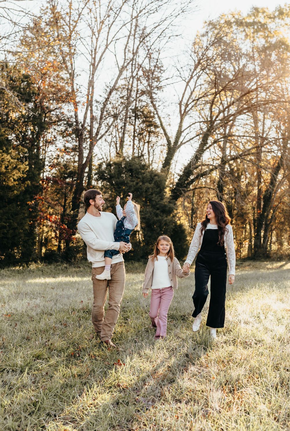 A family shares candid moments together in a sunlit field with autumn trees.
