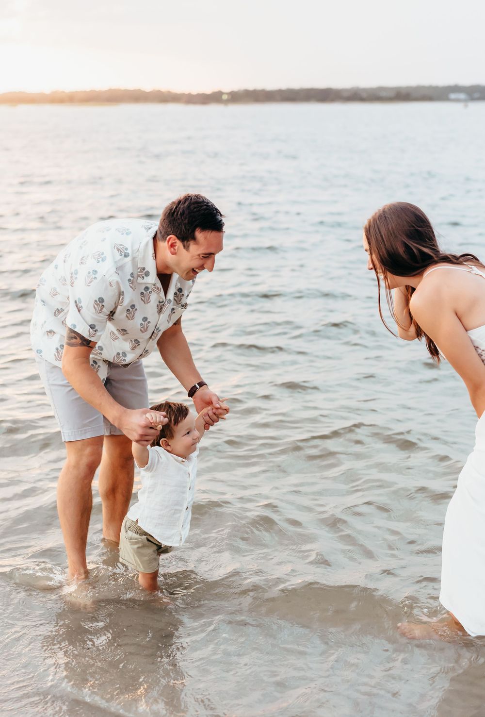 Family playing together in shallow ocean waves at sunset.