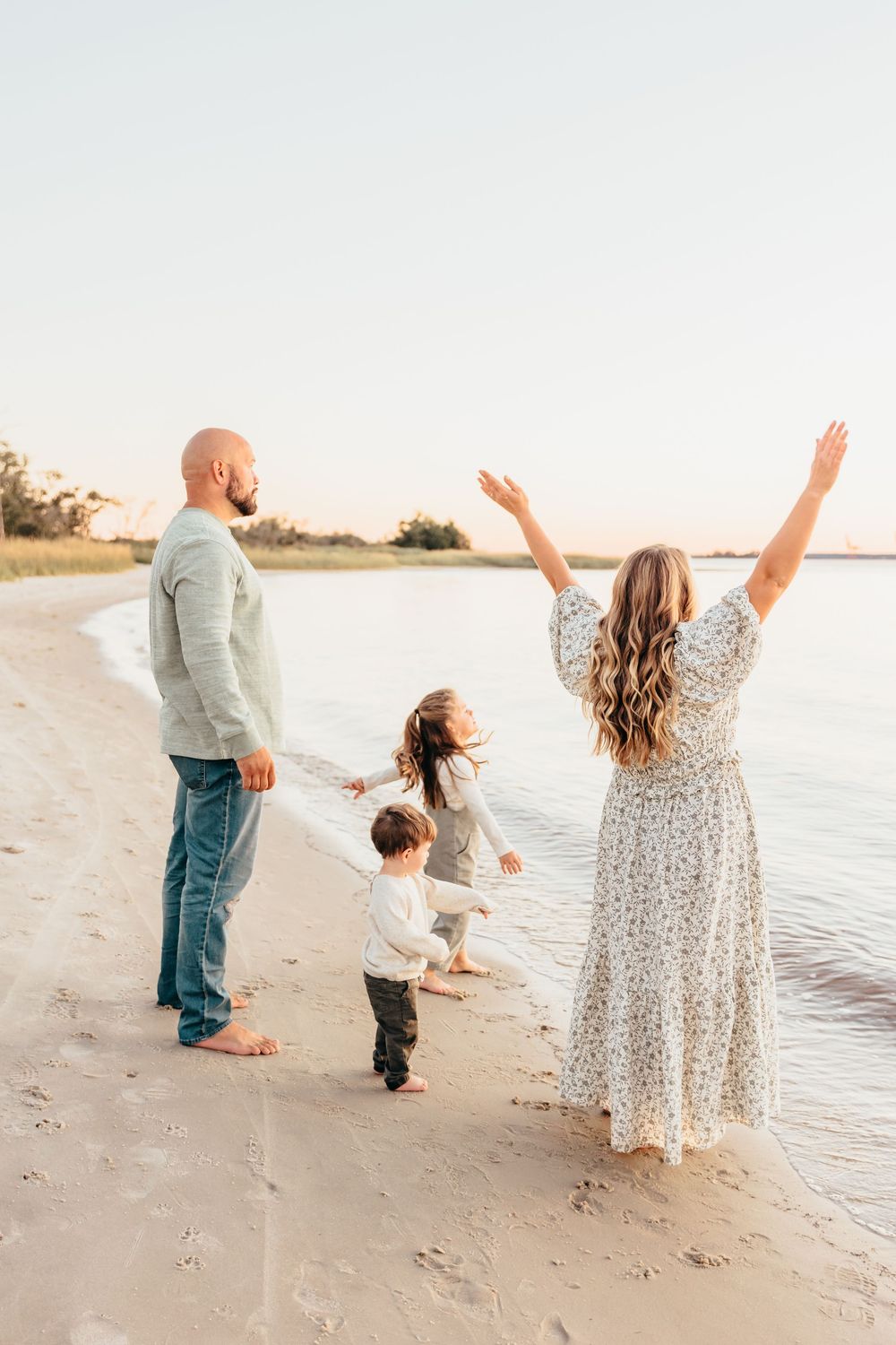 Family celebrating with raised arms on beach at golden hour.