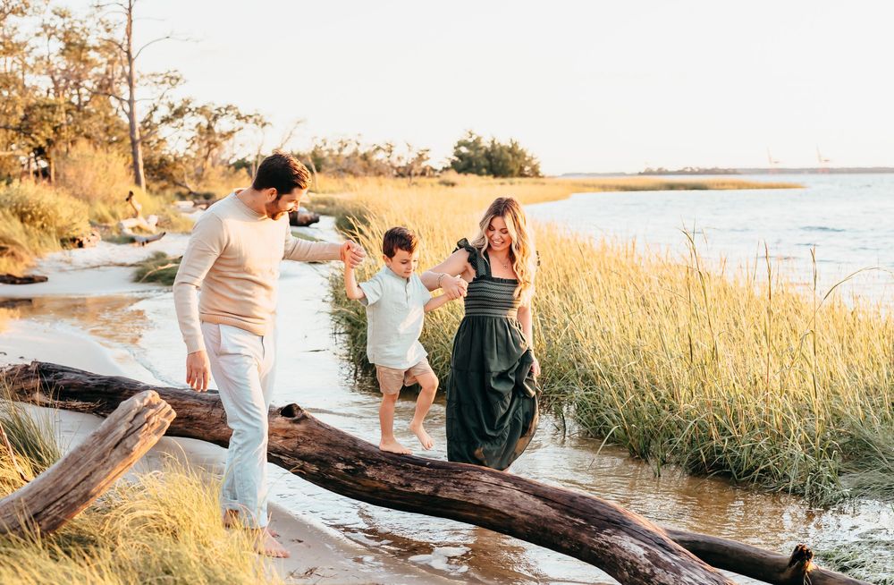 Family members carefully crossing a large piece of driftwood on a coastal beach trail.