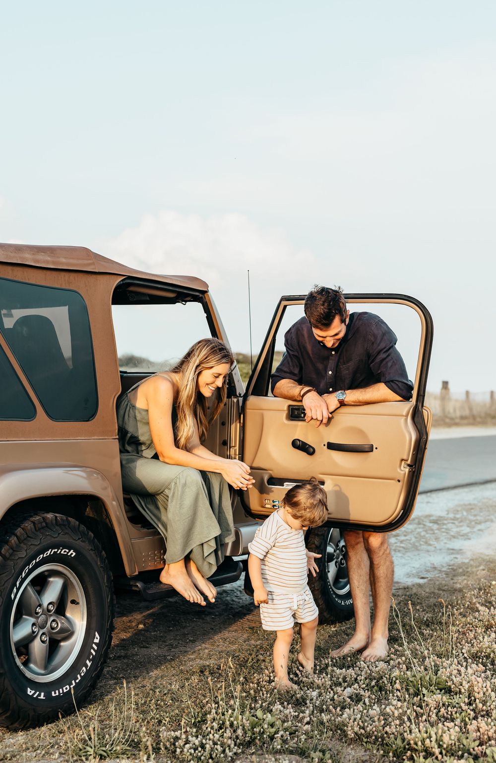 A family gathering around a brown Jeep in an outdoor setting.