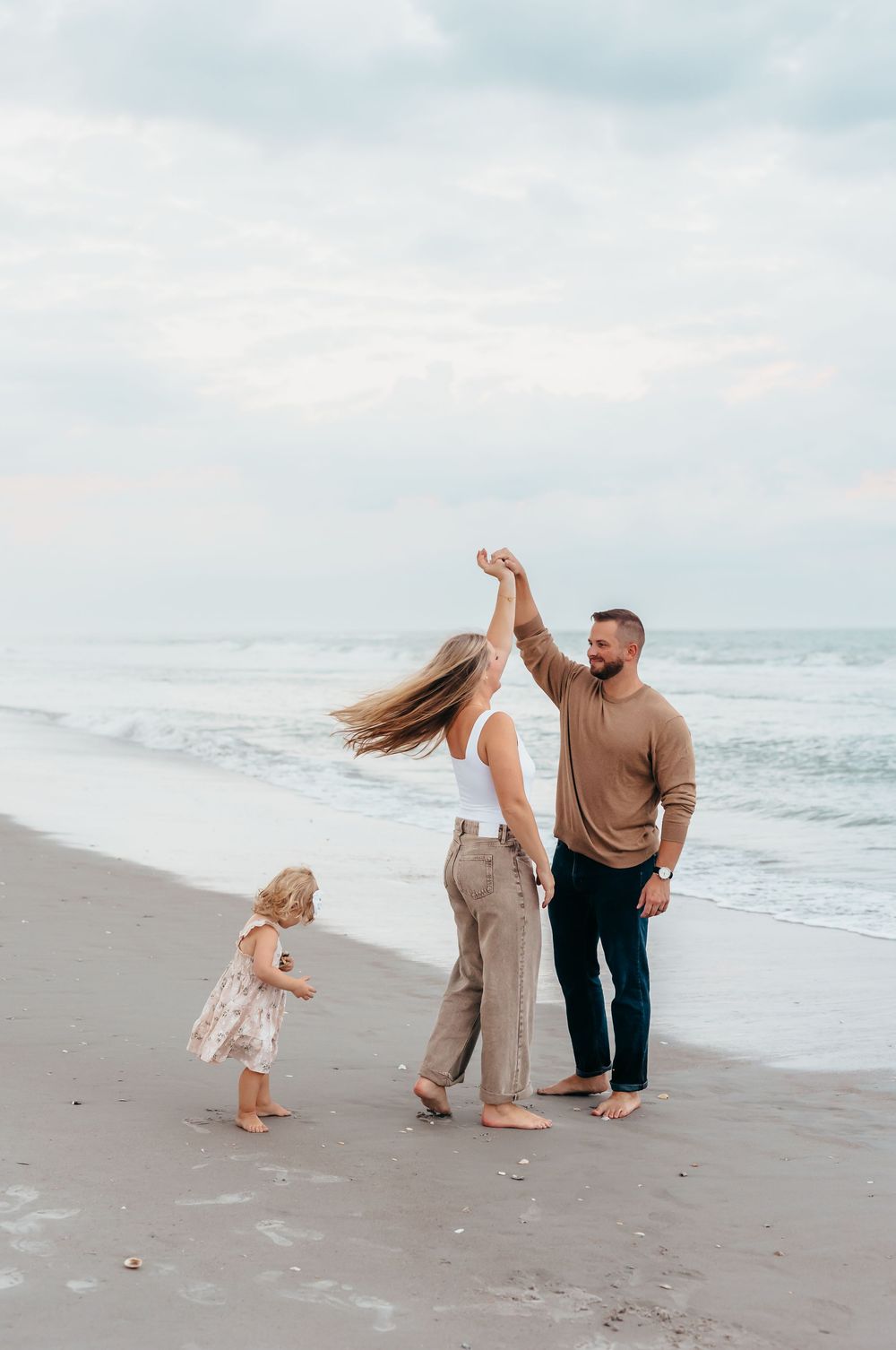 A family enjoys playful moments together on a cloudy beach day.