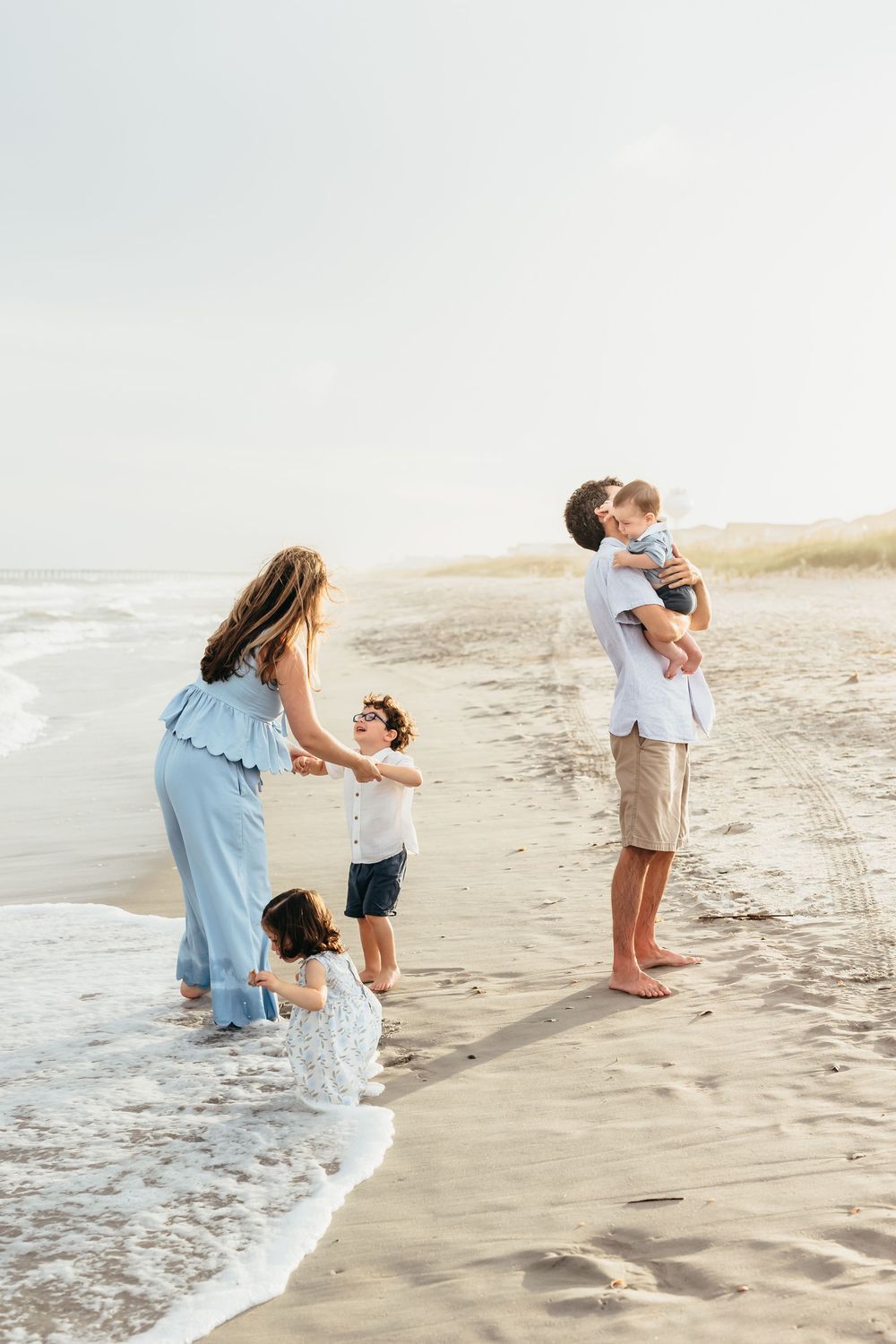 A family plays together at the edge of the ocean waves on a sandy beach. Wilmington NC.
