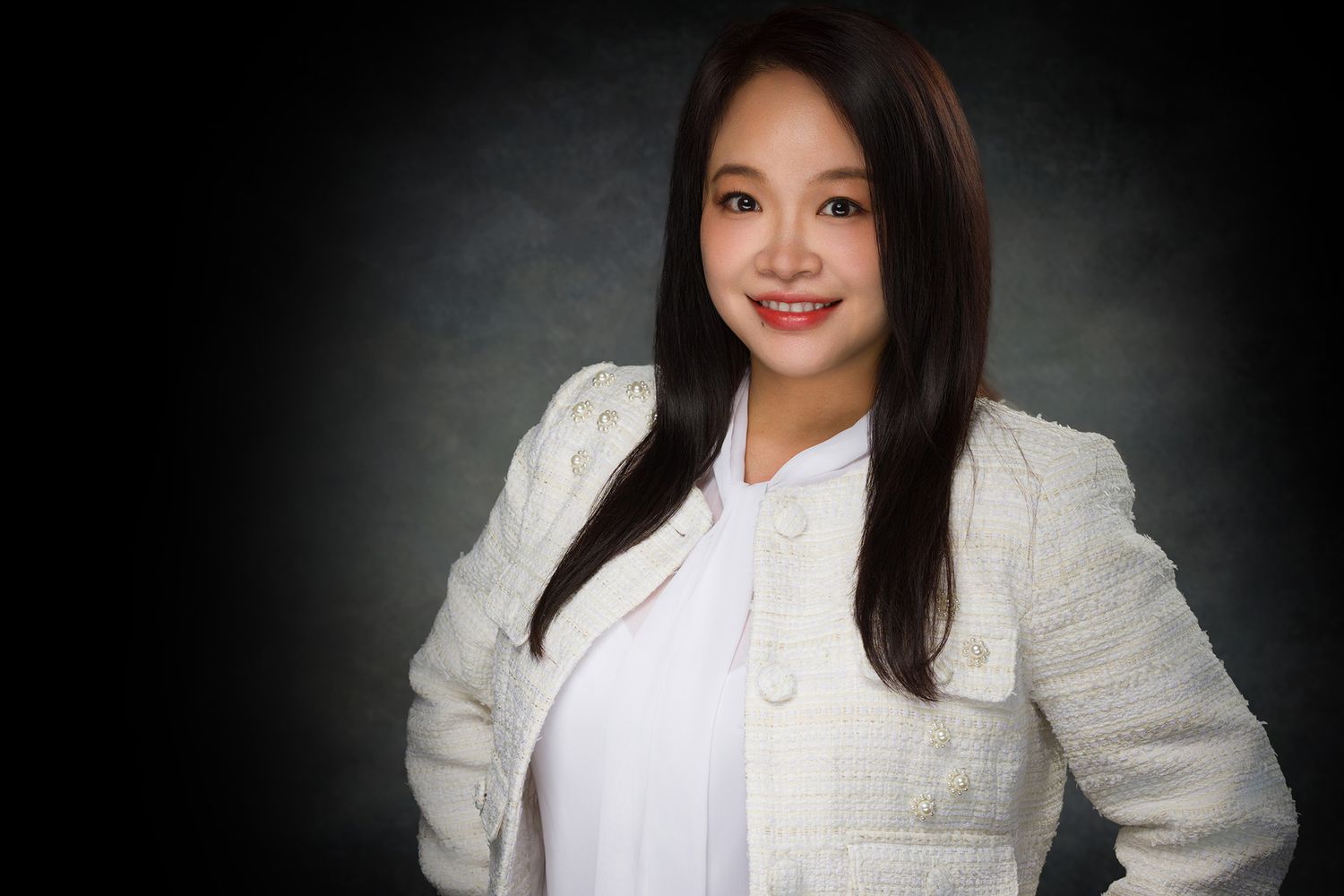 Professional studio portrait of someone wearing a white blazer and top against a dark background with dramatic lighting.