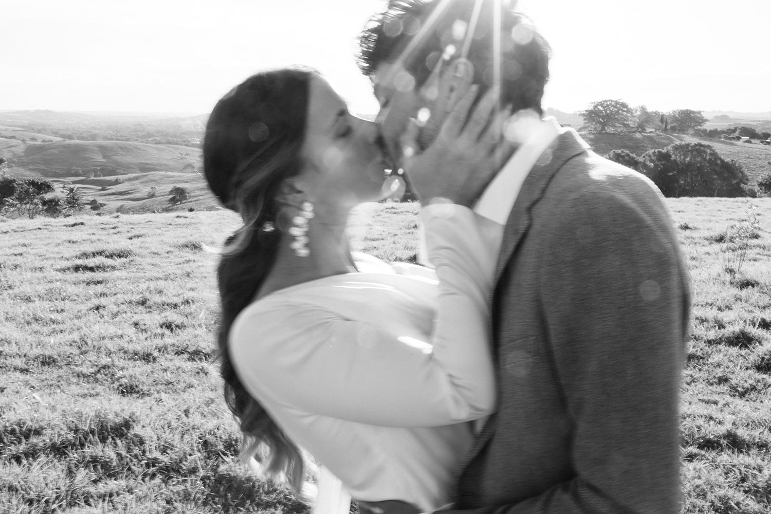 A romantic couple shares a tender kiss on a hillside in black and white photography.
