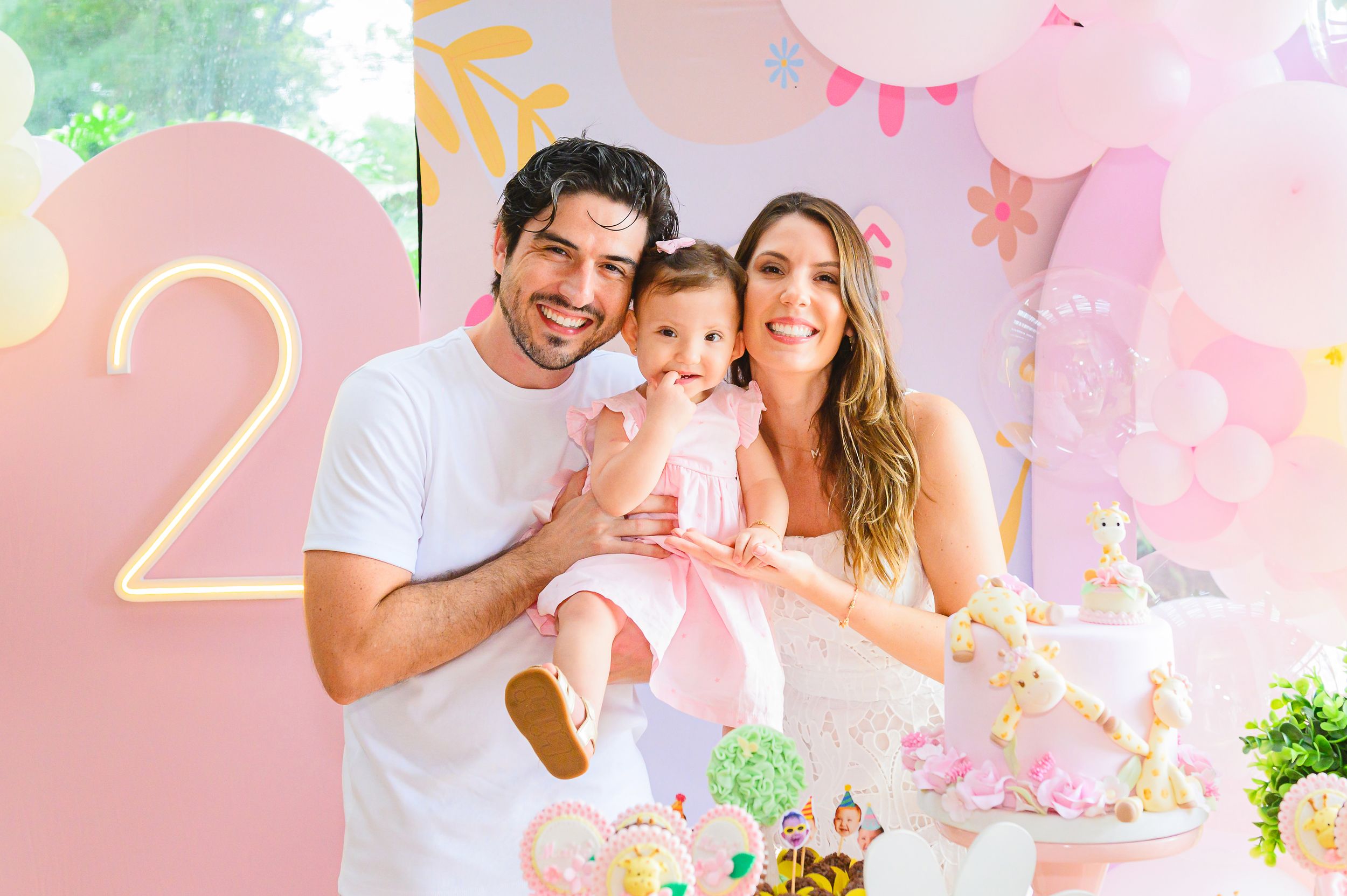 A pink and pastel birthday party celebration with the number 2 displayed against a decorated wall backdrop with balloons.