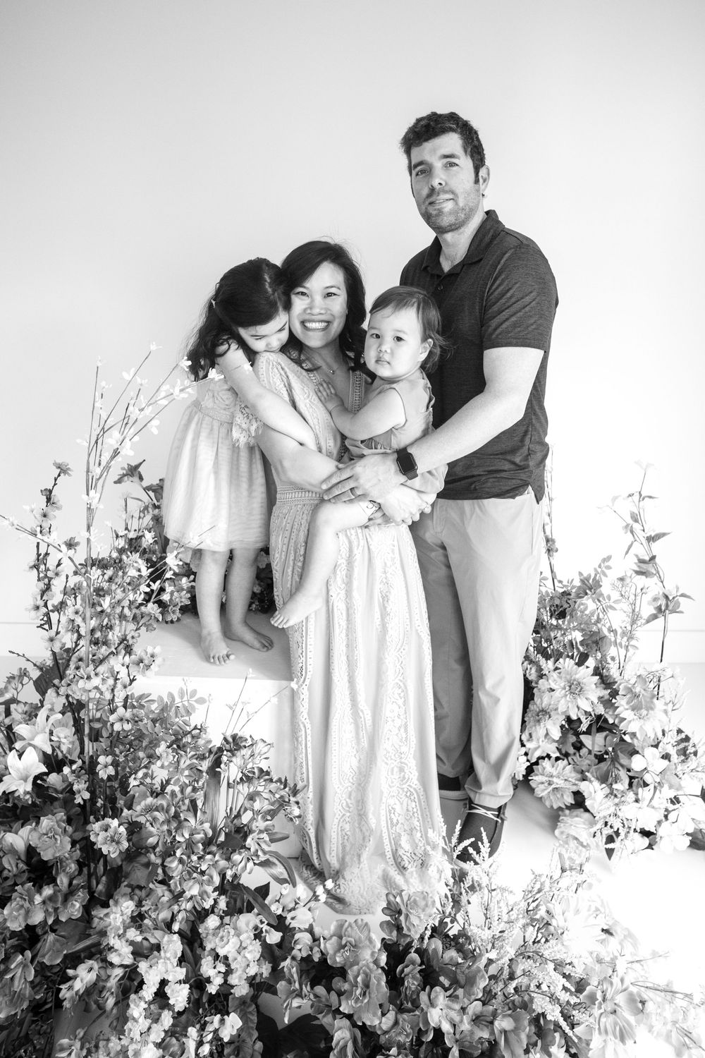 Family of four poses together in a black and white studio portrait with floral arrangements. Taken at Studio 428 in Leesburg Va