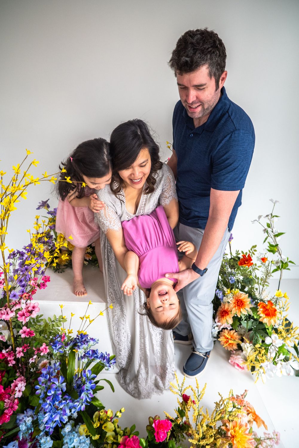 A family plays and laughs together surrounded by colorful spring flowers like delphiniums, forsythia and wildflowers.