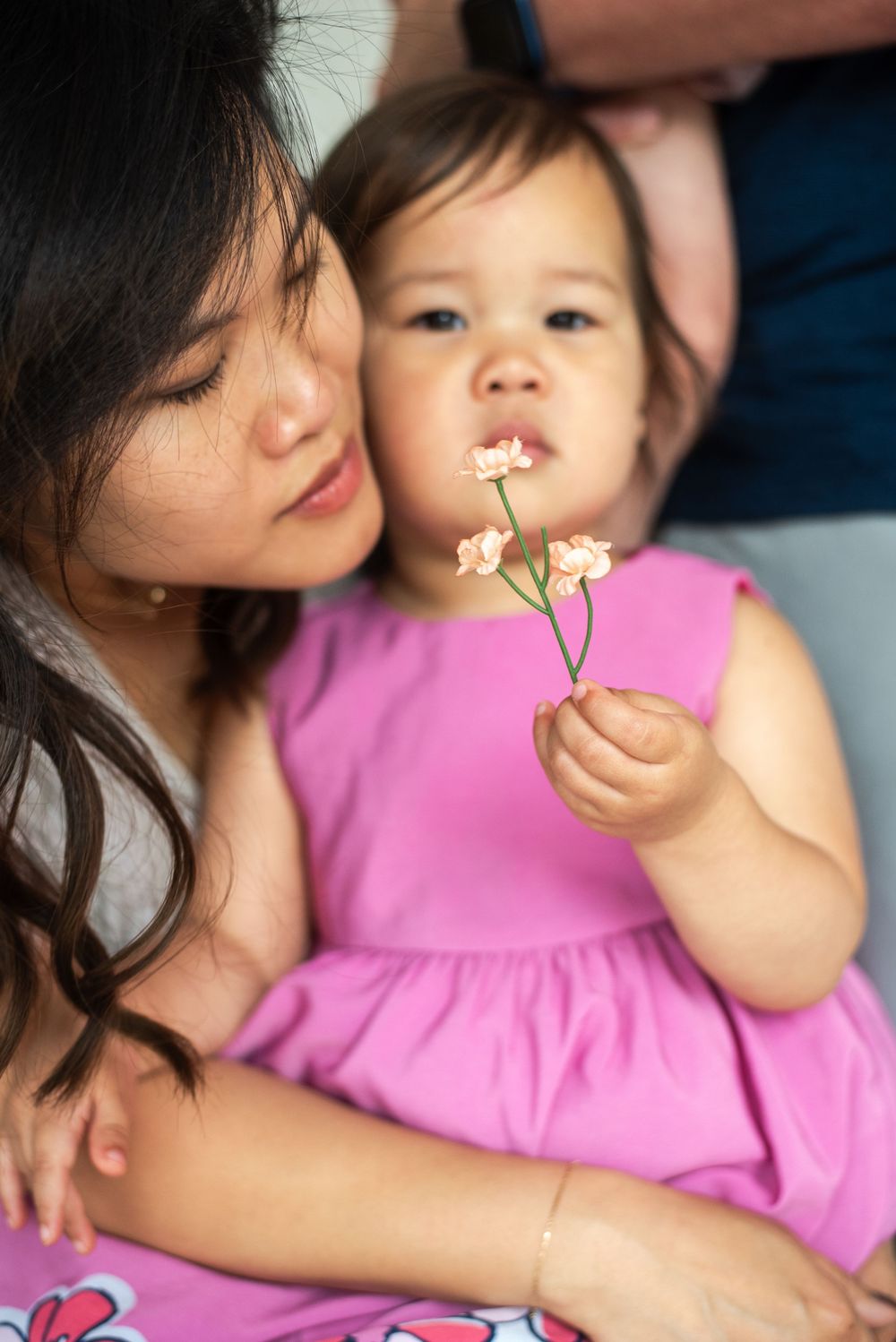 A tender family moment shows a parent and child in pink sharing delicate white flowers while relaxing together. Taken at Studio 428 in VA
