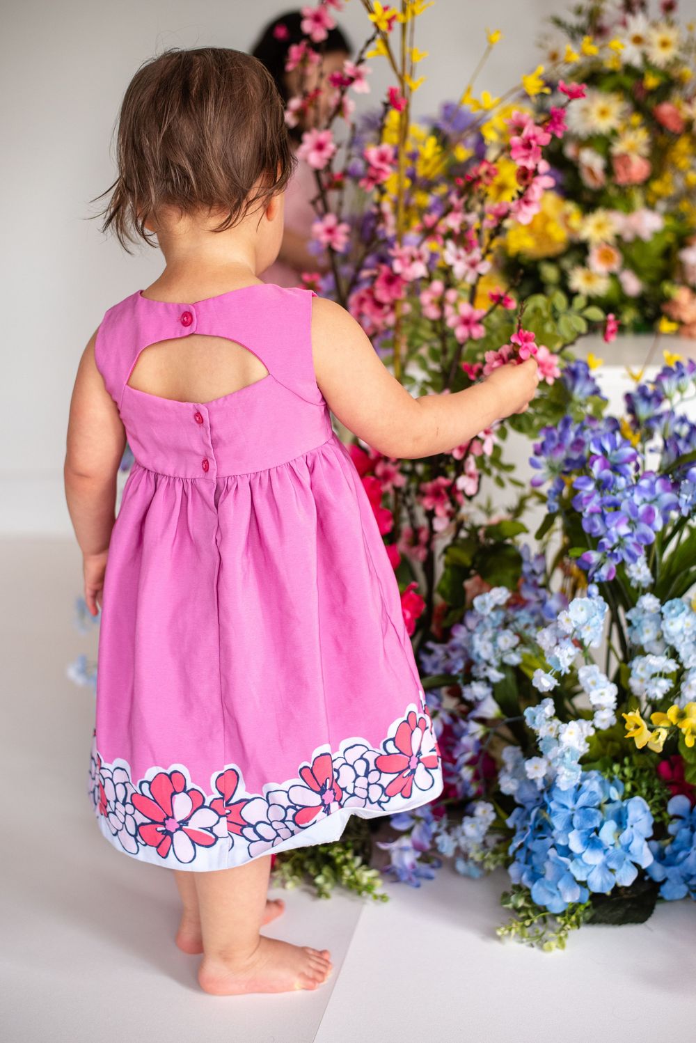 A pink dress with floral trim is worn by someone standing near a colorful spring flower arrangement. Taken at Studio 428 in Leesburg Va