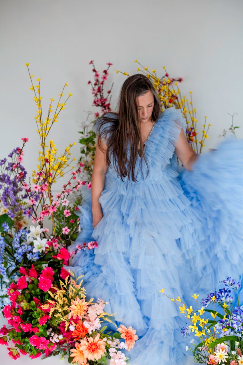 Ethereal blue tulle gown surrounded by vibrant spring flowers and colorful floral arrangements against light backdrop.