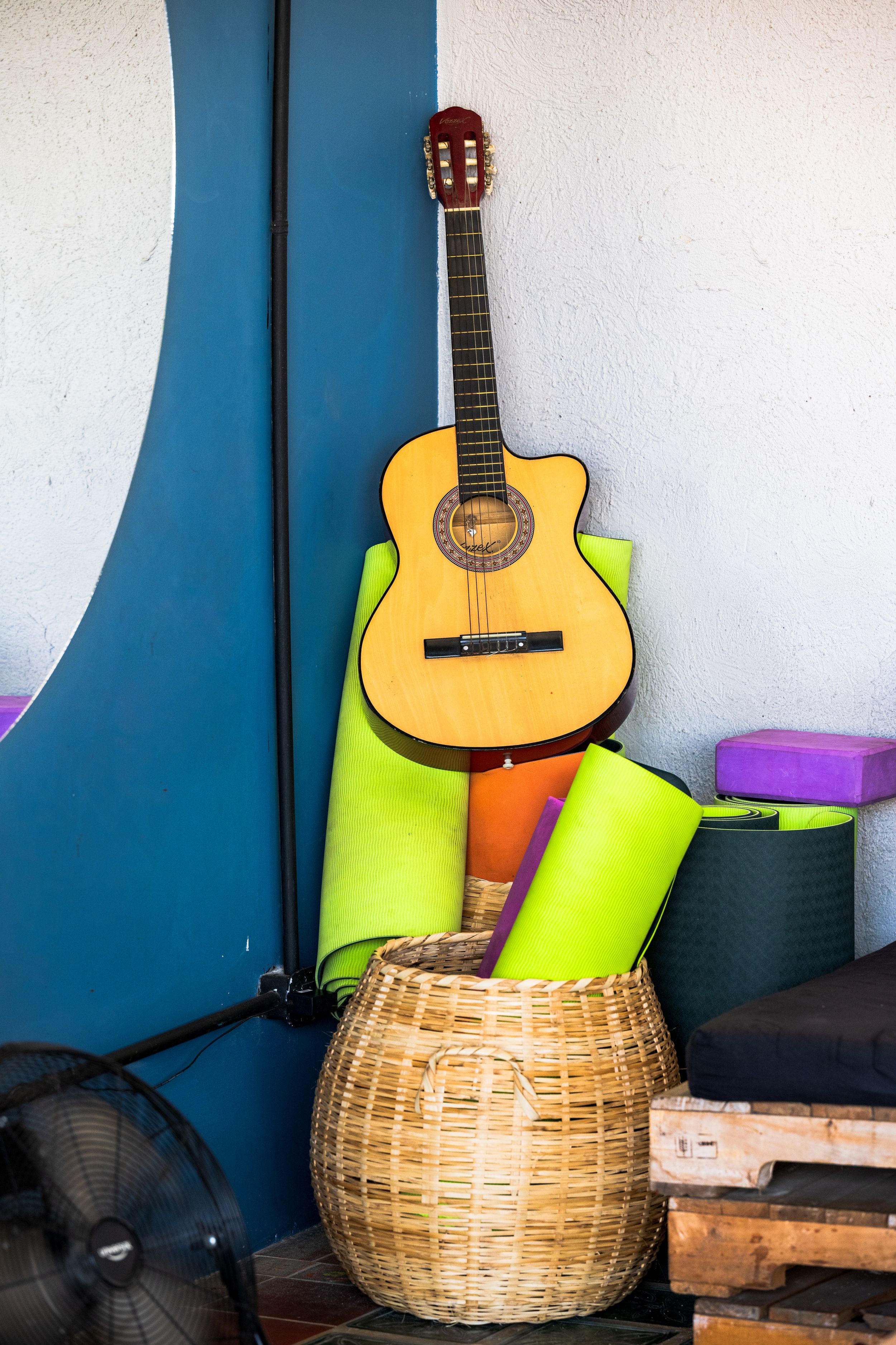 An acoustic guitar rests against colorful foam rolls in a woven wicker basket.