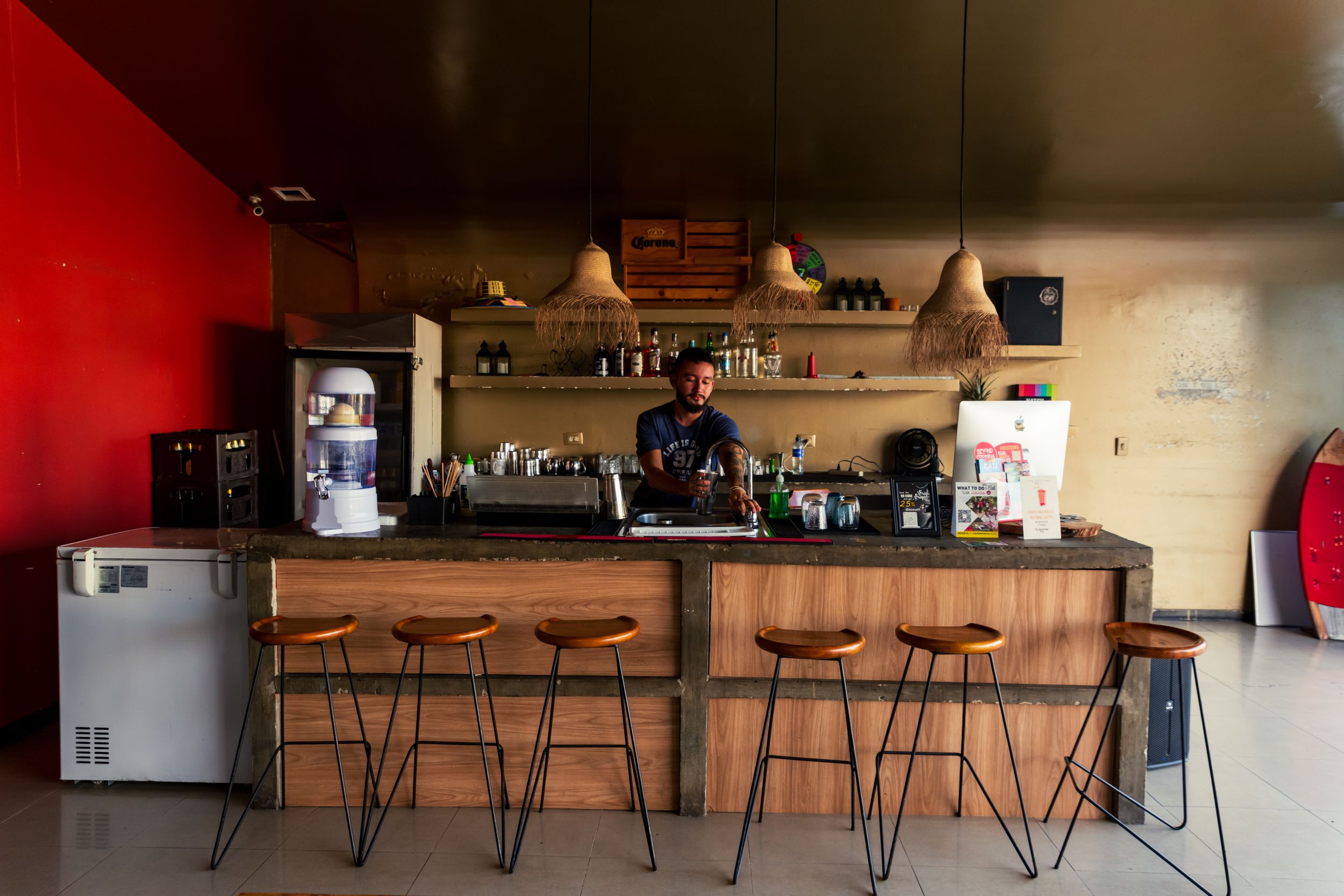 Modern coffee shop interior with wooden bar counter, industrial style stools, and floating shelves against a red accent wall.