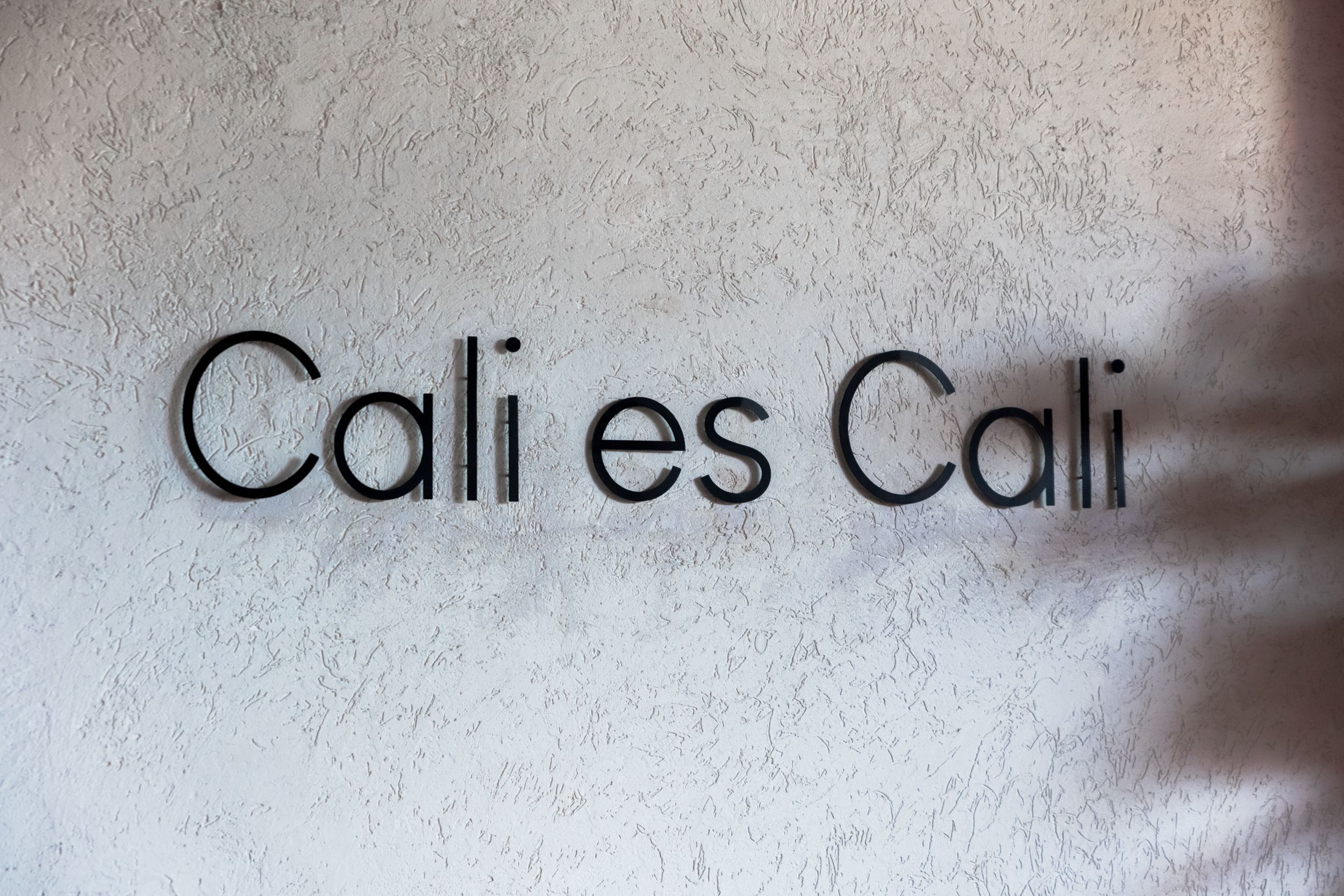 Black text reading "Cali es Cali" mounted on a textured white wall with subtle shadows.