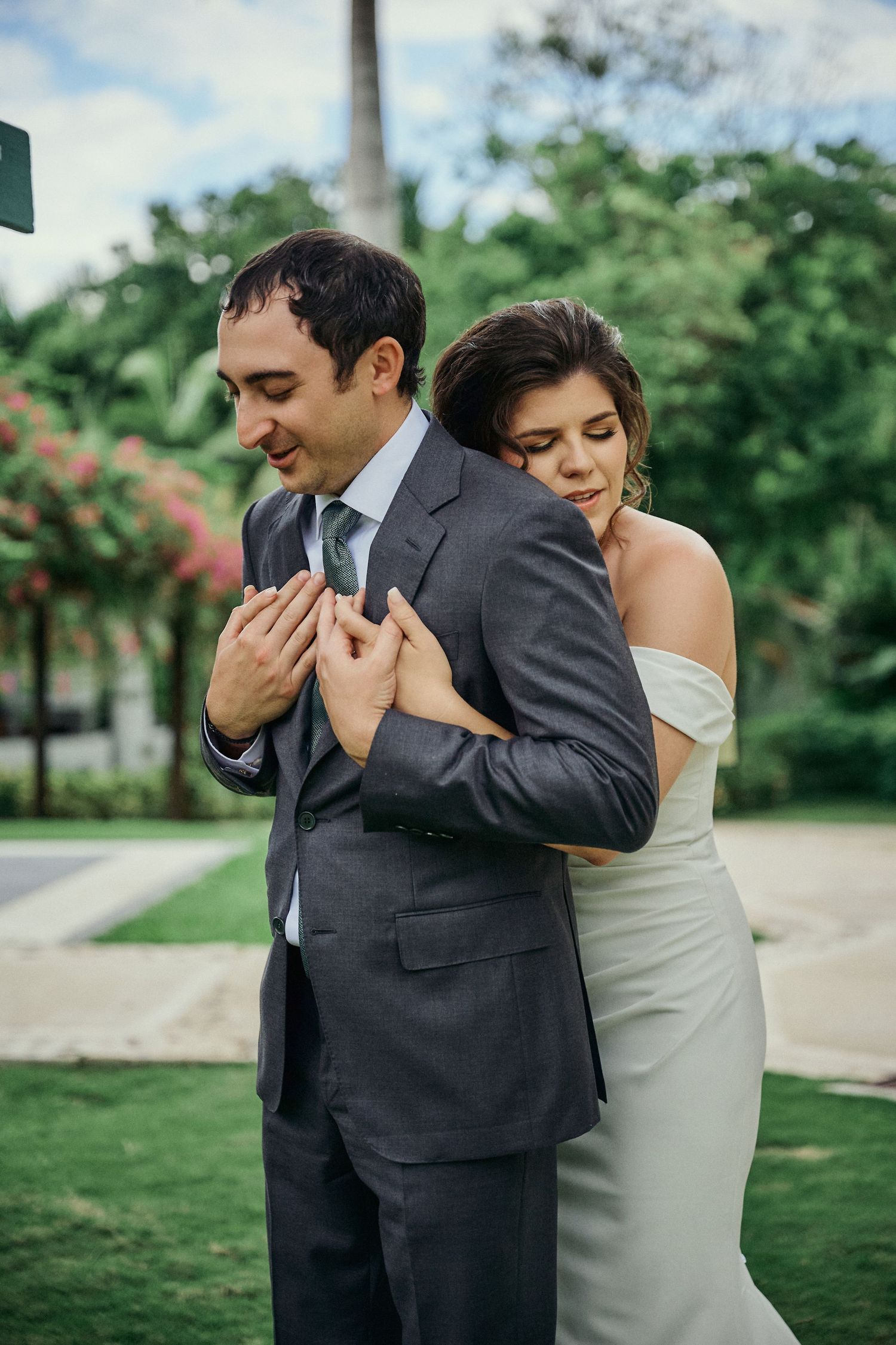Wedding couple stands by waterfront with palm trees and resort buildings in background . Jamaica Wedding Photographer