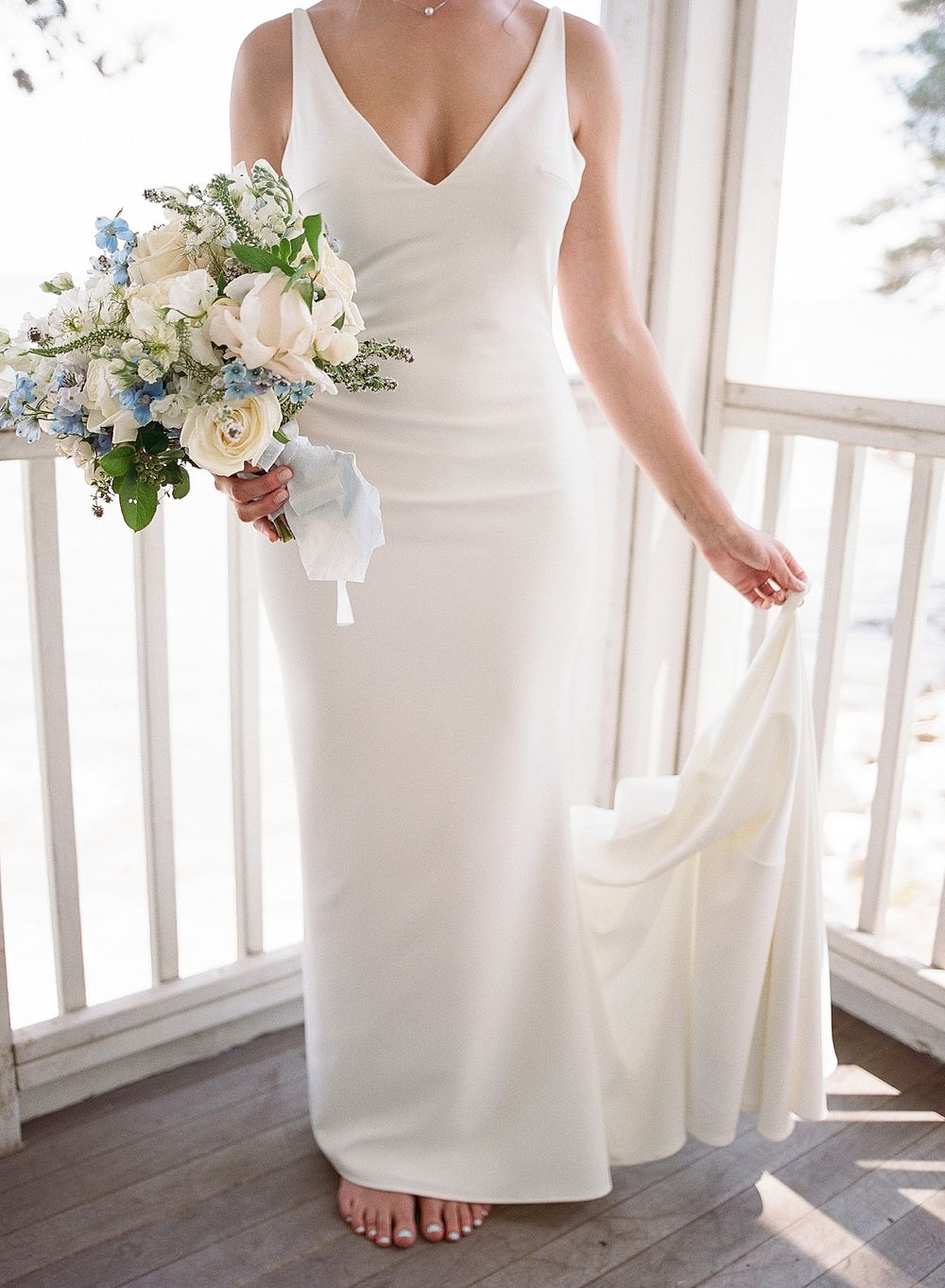 Elegant white wedding dress with v-neckline and fitted silhouette shown with delicate blue and white floral bouquet.