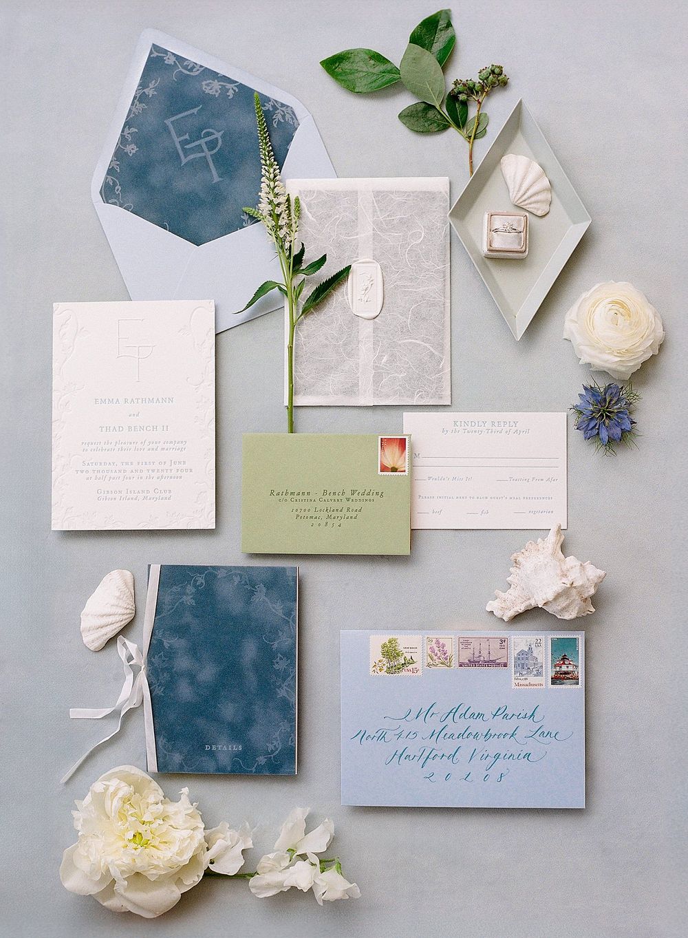 Elegant wedding stationery suite in blue and white with floral accents, envelopes and delicate blooms on grey background.