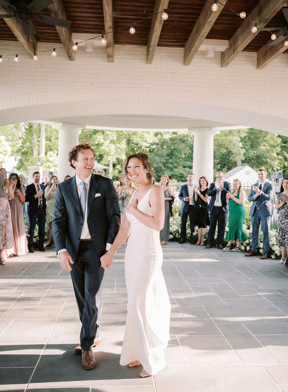 A couple smiles and laughs together during their first dance at an elegant covered outdoor wedding reception venue.