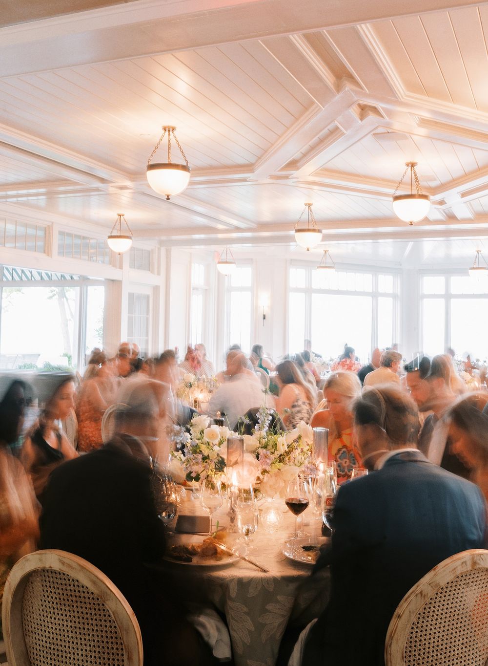 Elegant wedding reception in a bright room with coffered ceilings, round tables, and globe pendant lights.